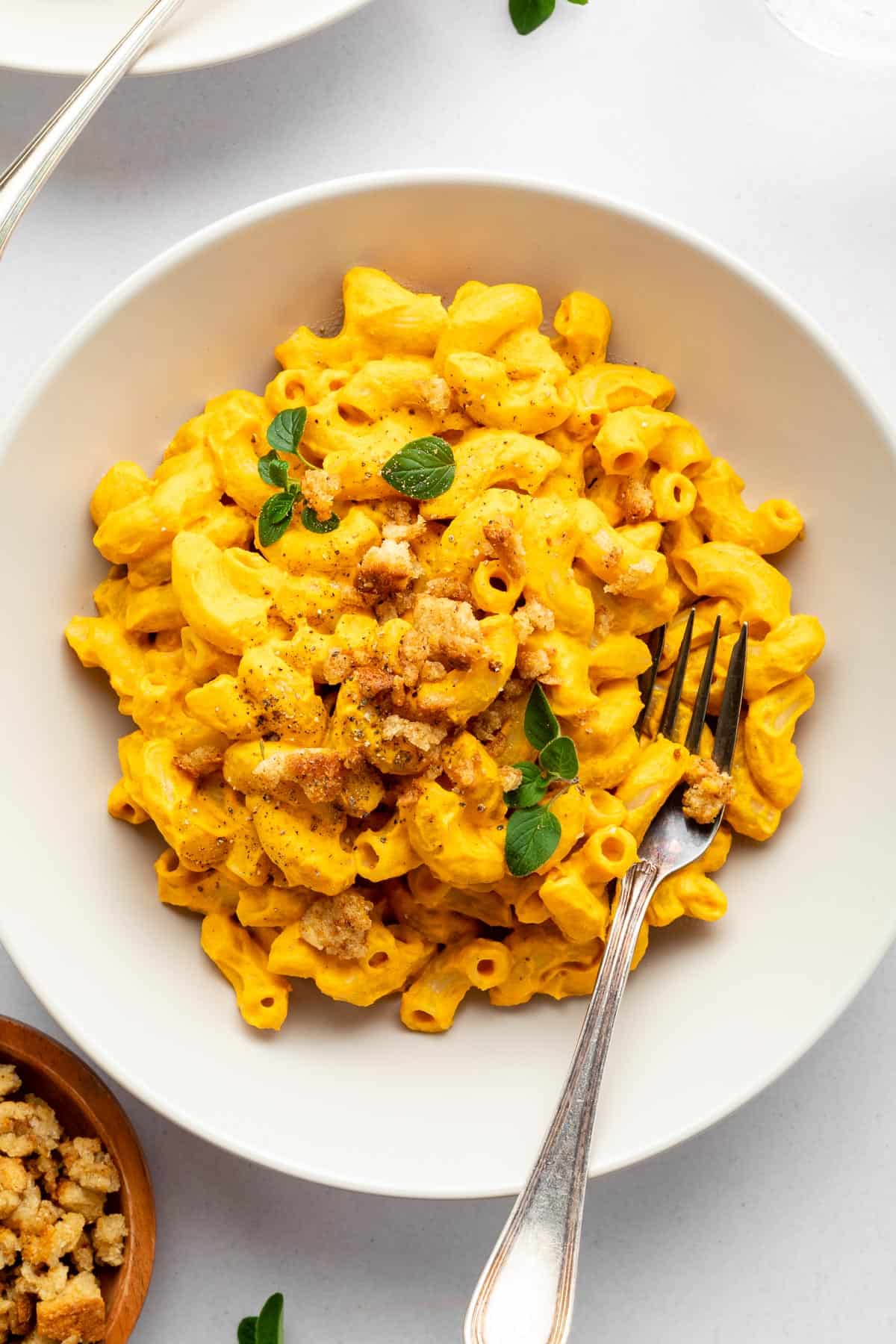 two bowls of vegan mac and cheese beside a bowl of cashews and a bowl of nutritional yeast