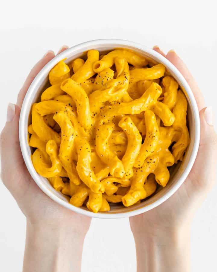 hands holding a white bowl filled with vegan mac and cheese