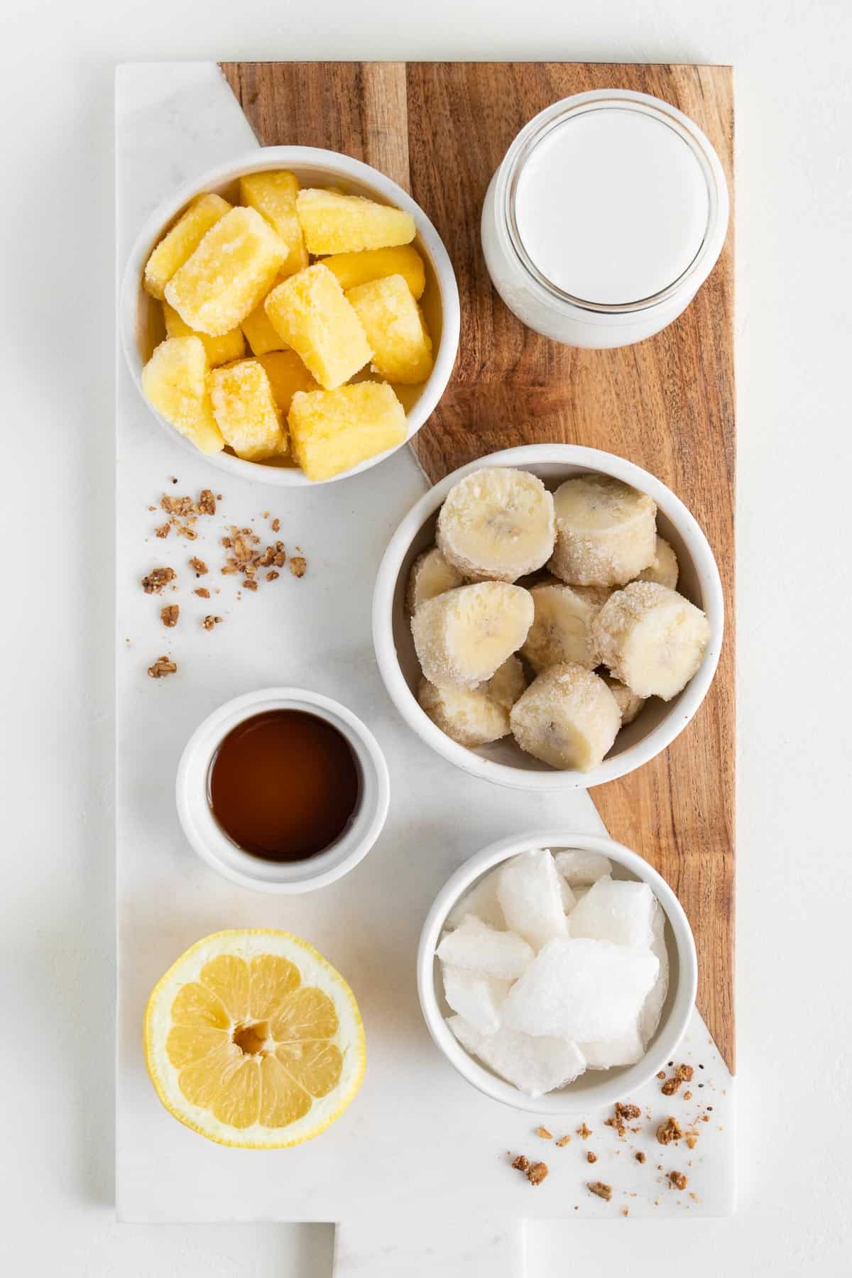 a marble wooden board topped with bananas, pineapple, maple syrup, lemon juice, coconut chunks, coconut milk, and a lemon