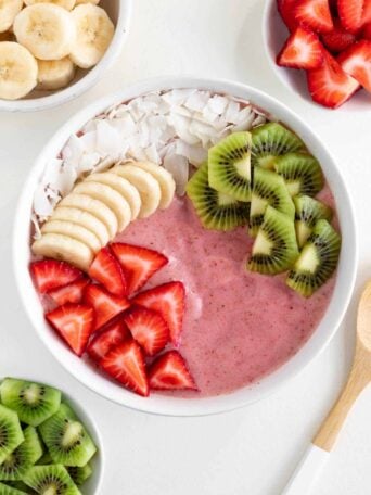 a strawberry kiwi smoothie bowl surrounded by bowls of sliced banana, strawberries, and kiwi fruit