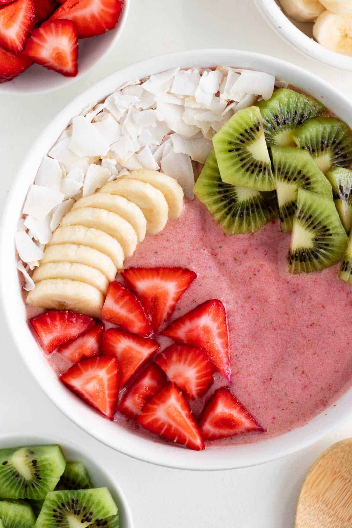 a strawberry smoothie bowl topped with coconut flakes, banana, kiwi fruit, and berries