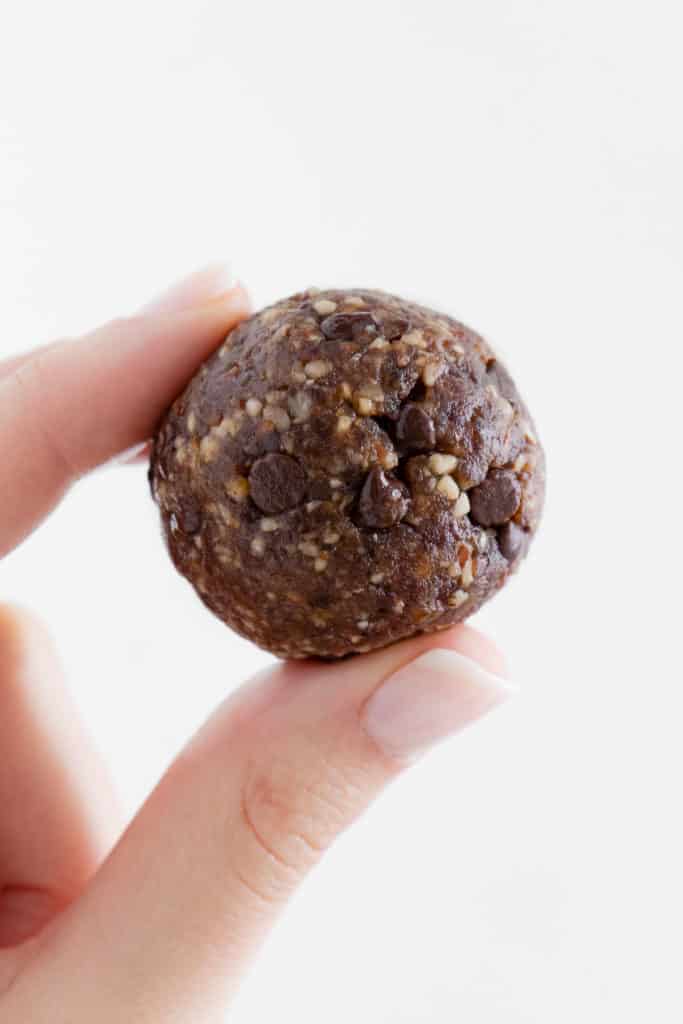 a hand holding one turtle energy ball with chocolate chips