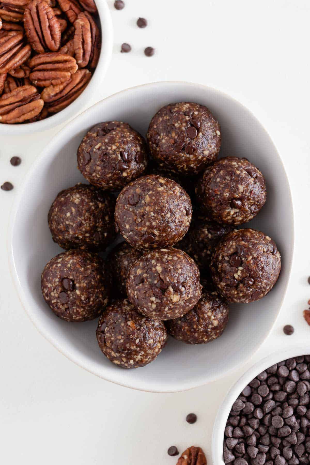 turtle energy balls inside a white bowl beside a bowl of pecans and medjool dates