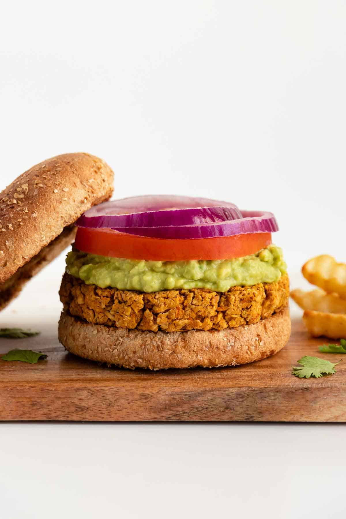 a vegan chickpea burger patty on a bun with mashed avocado, tomato, and sliced red onion