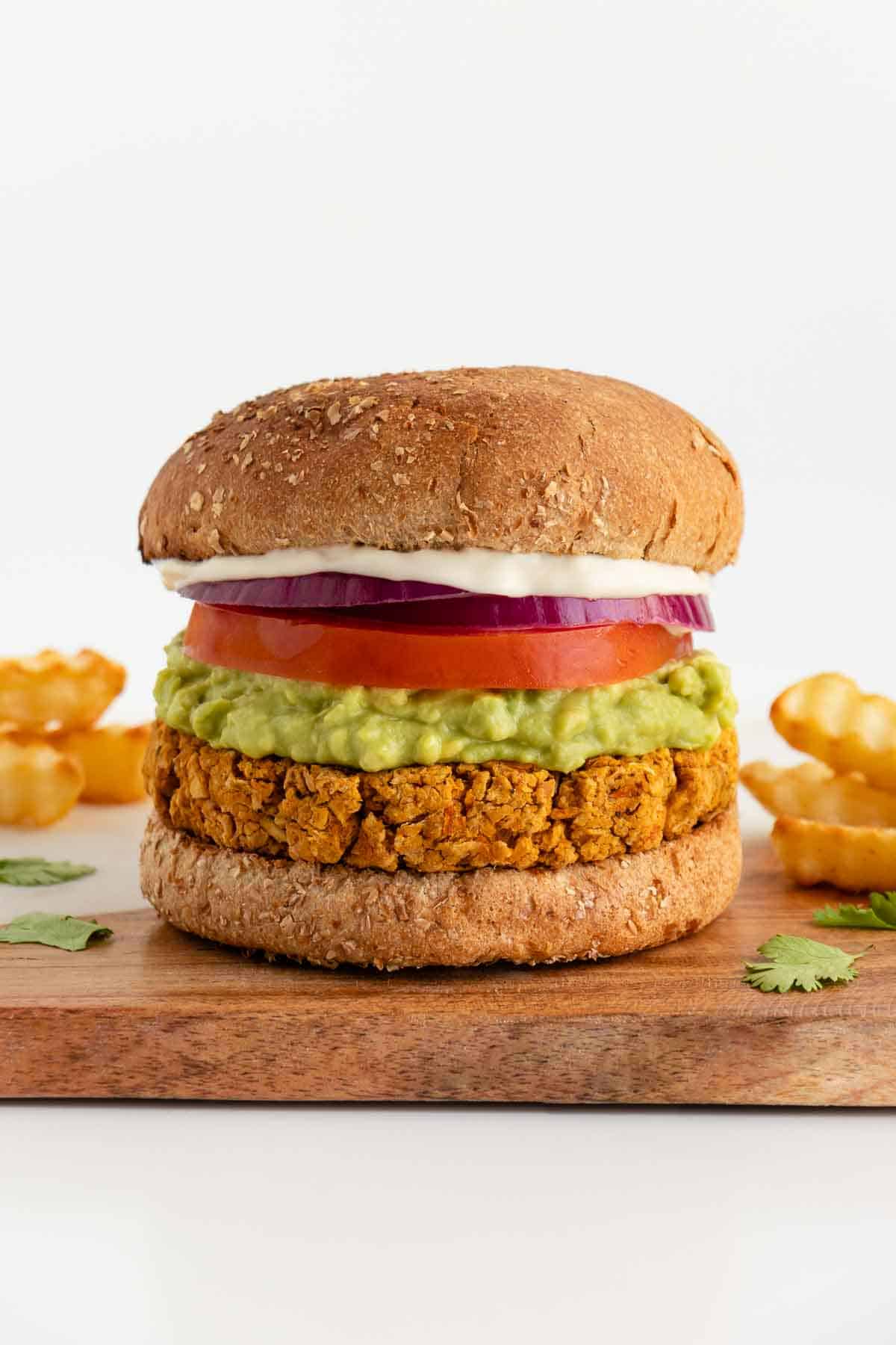 a vegan chickpea burger between two buns with mashed avocado, tomato, red onion, and mayo surrounded by crinkle cut french fries
