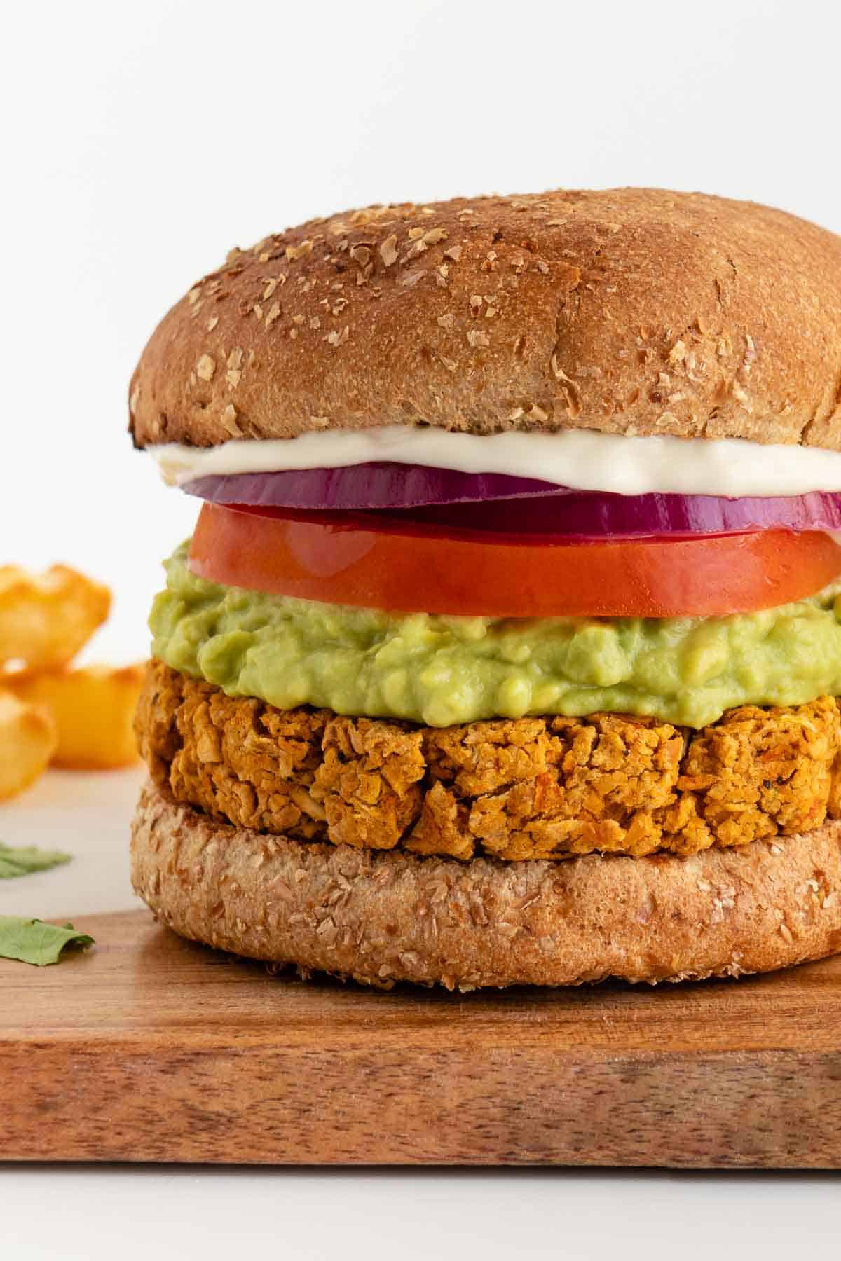 a vegan chickpea burger between two buns with mashed avocado, tomato, red onion, and mayo surrounded by crinkle cut french fries