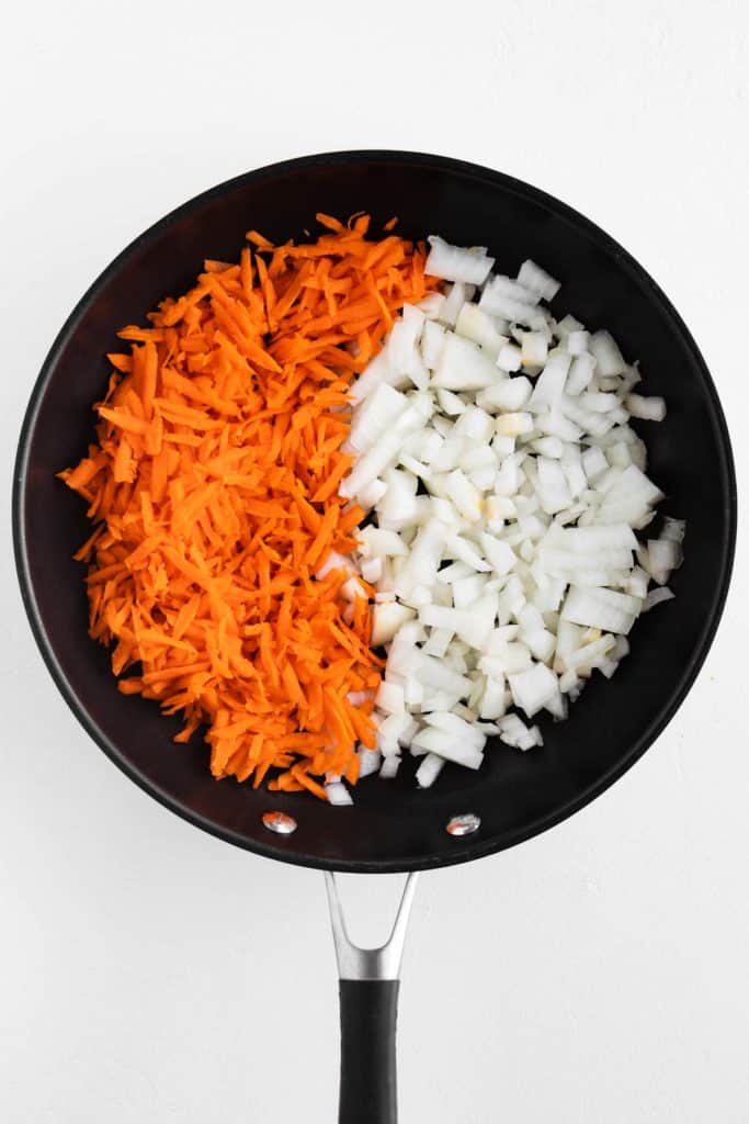 shredded carrot and diced onion in a black frying pan