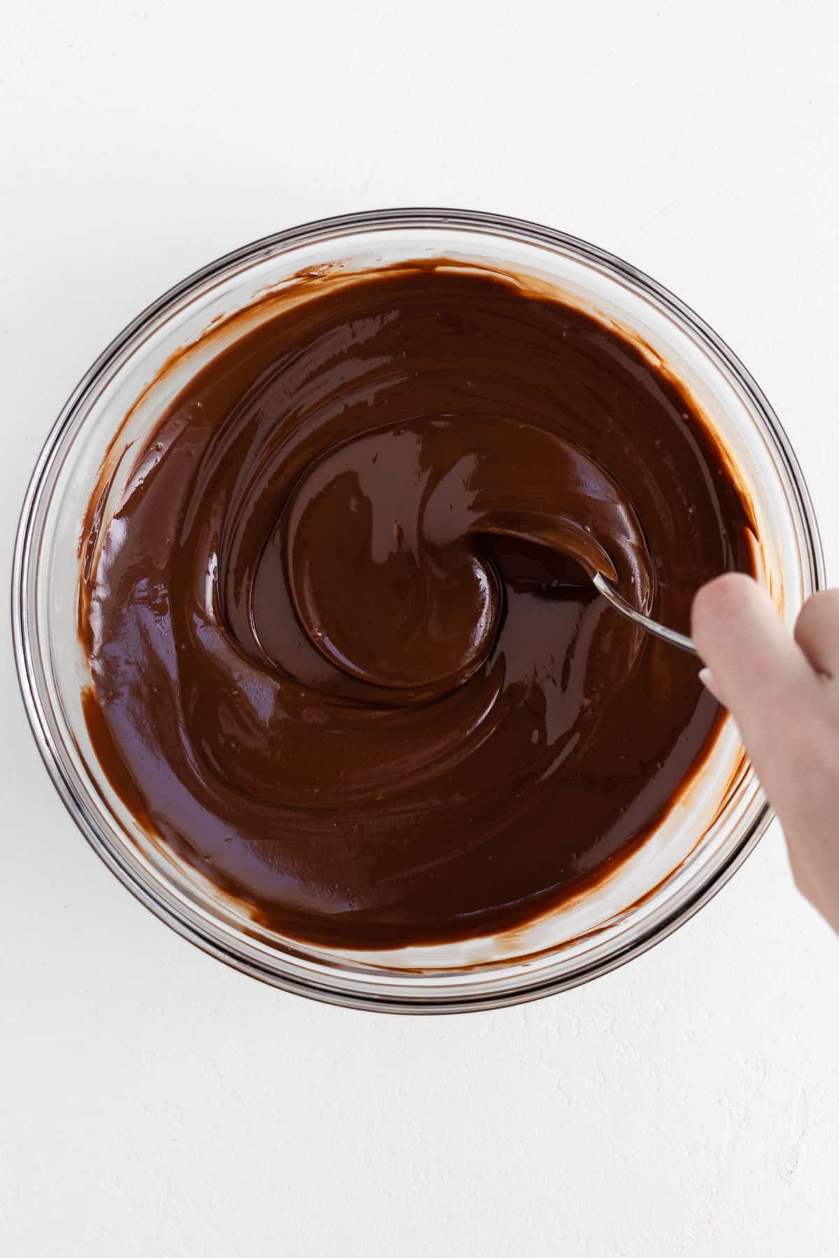 a hand mixing melted chocolate in a large glass bowl