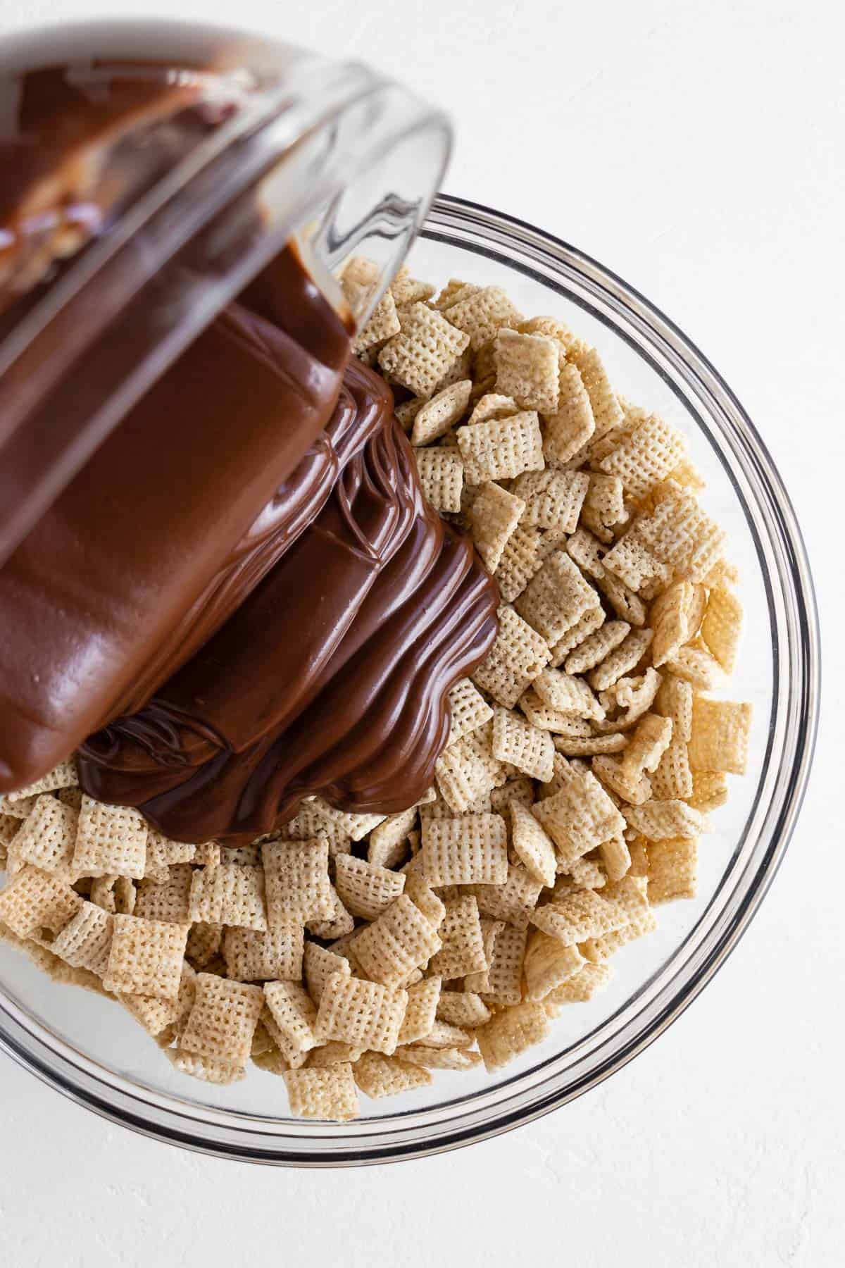 melted chocolate being poured over a bowl of chex cereal