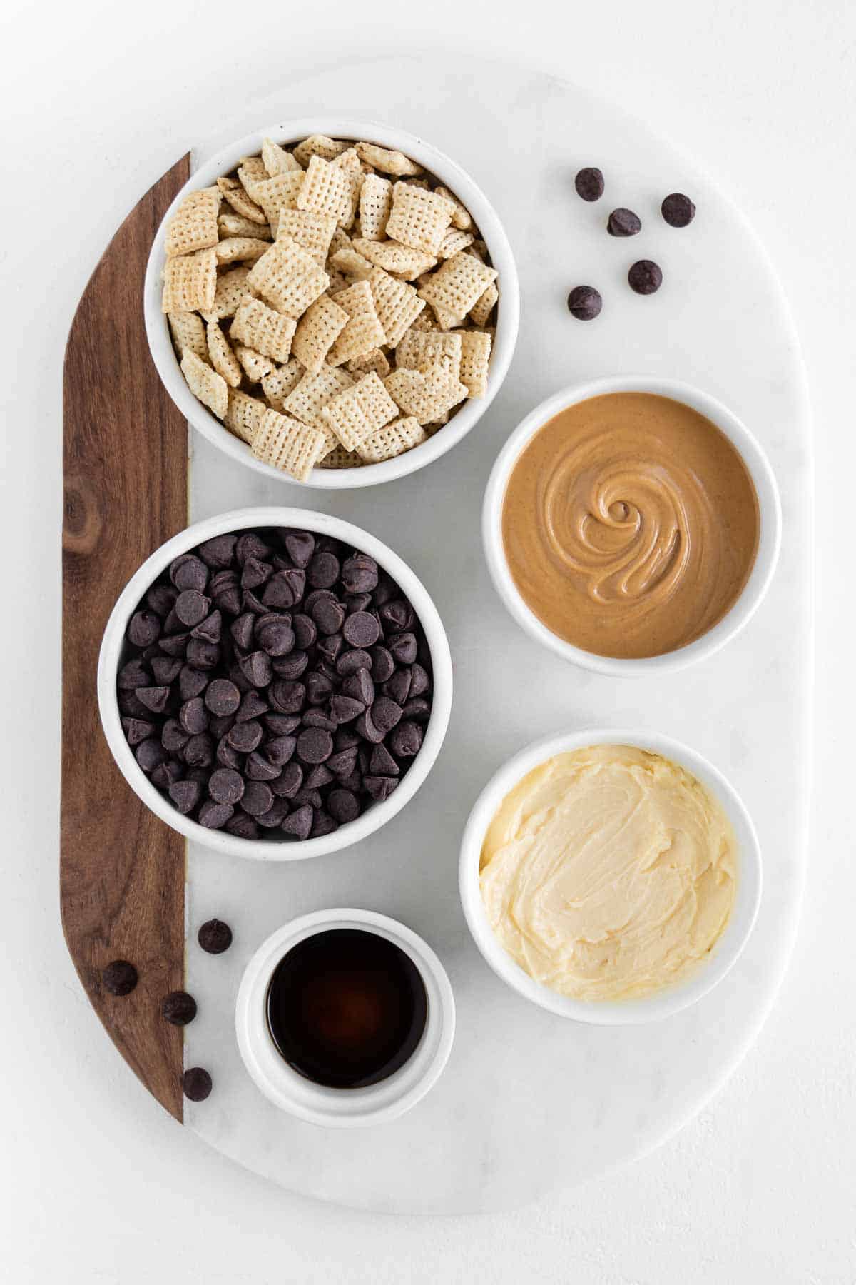 a marble board topped with bowls of chex cereal, chocolate chips, peanut butter, butter, and vanilla extract