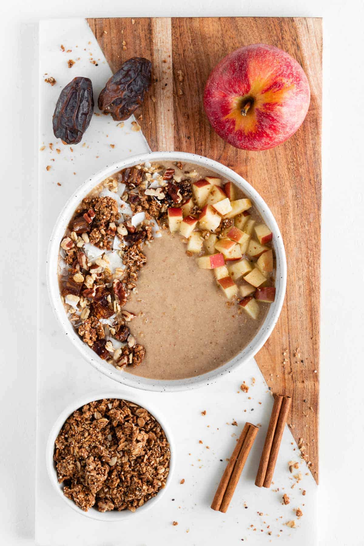 apple pie smoothie bowl, granola, apples, medjool dates, and cinnamon sticks on a marble board