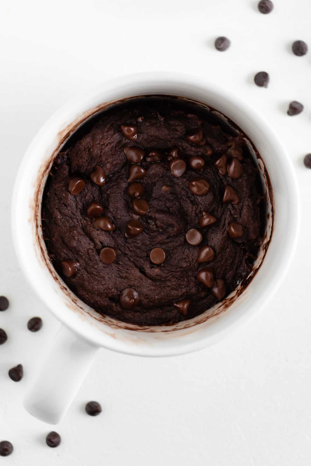 vegan chocolate brownie mug cake in a white mug, surrounded by mini chocolate chips
