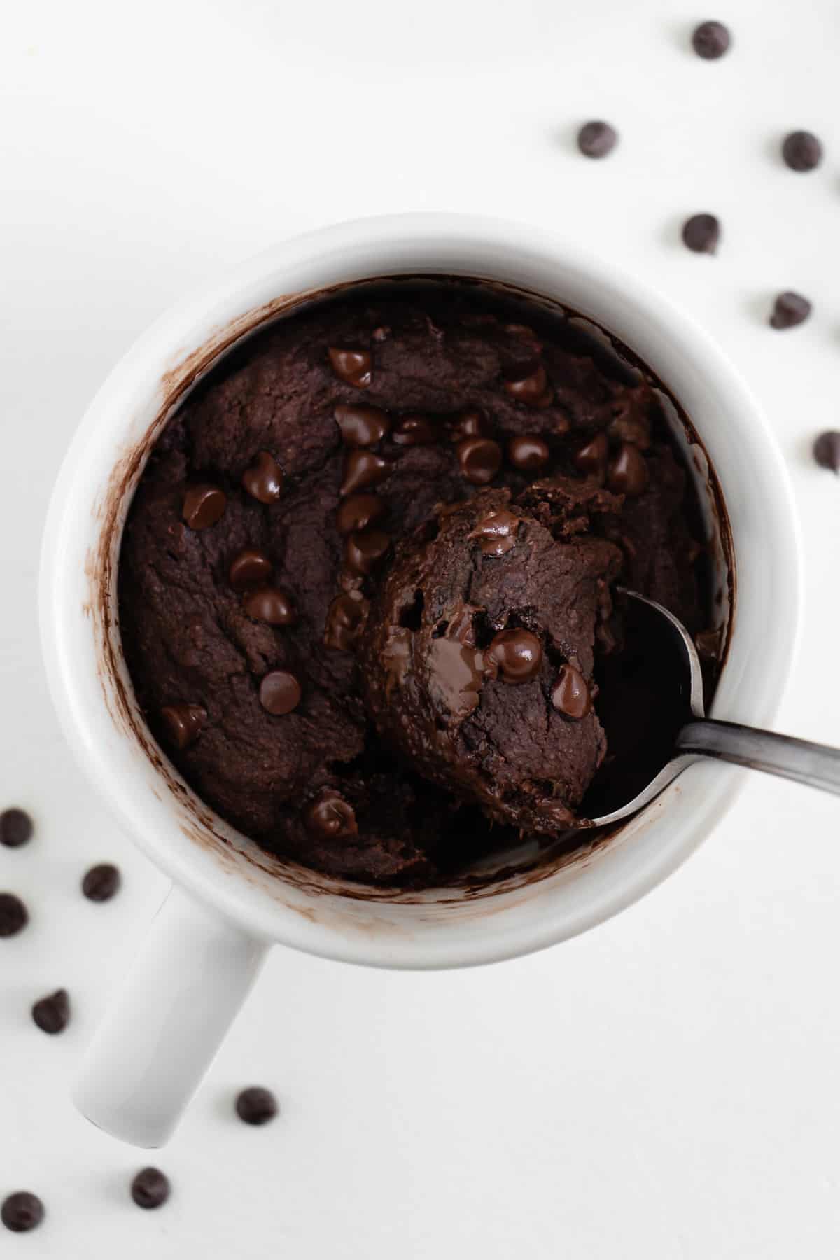a spoon digging into a vegan chocolate mugcake inside a white mug