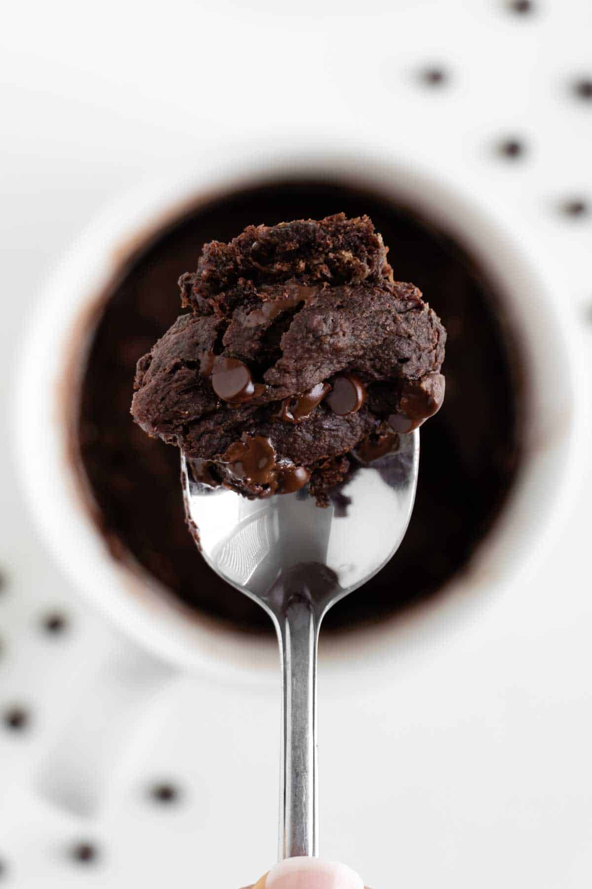 a spoon holding a scoop of a vegan chocolate banana mug cake