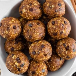 pumpkin energy balls in a white bowl surrounded by pumpkin puree, peanut butter, chocolate chips, and oats