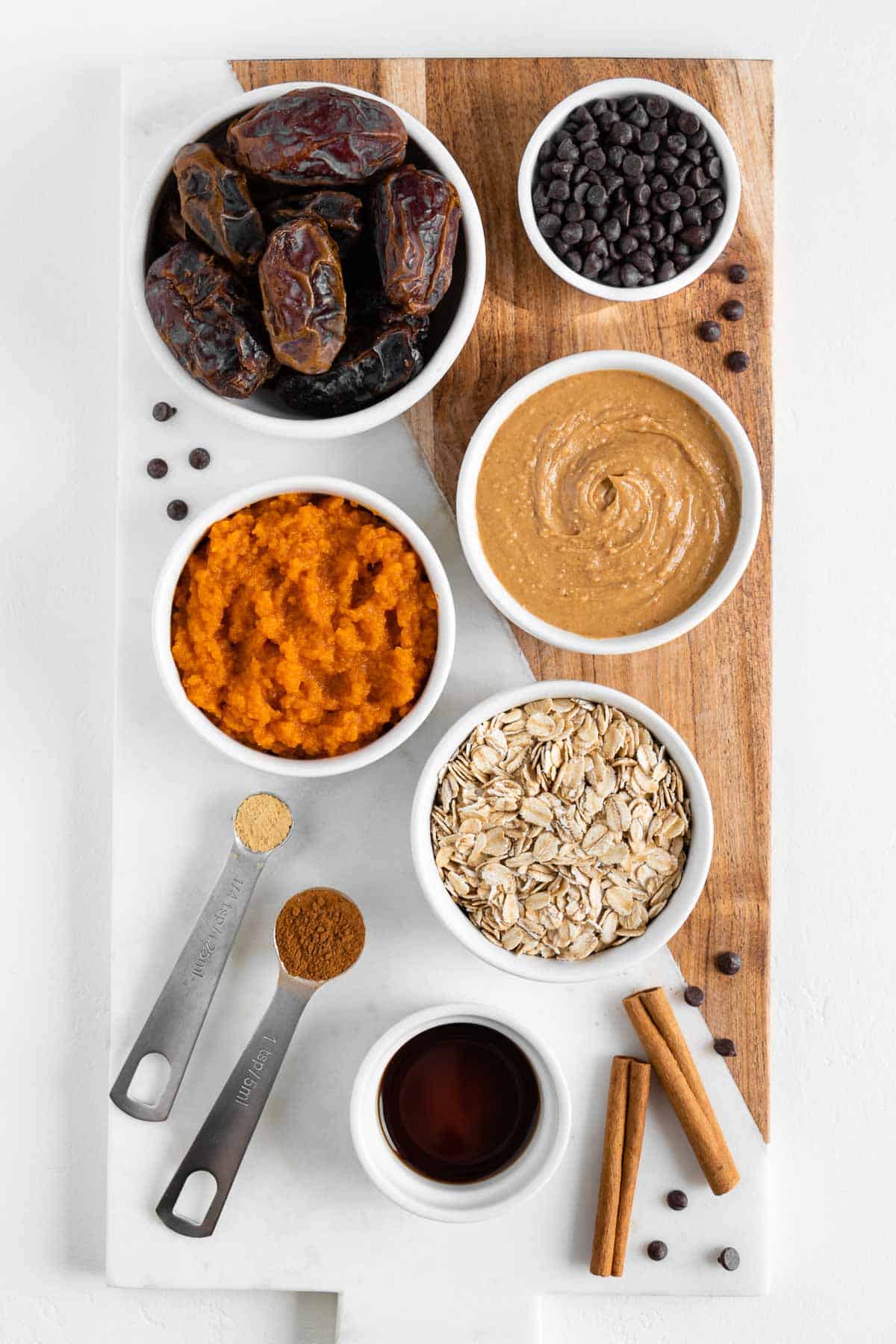 bowls filled with pumpkin puree, medjool dates, peanut butter, oats, vanilla extract, and chocolate chips on a wooden marble board