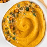 pumpkin hummus in a white bowl surrounded by roasted chickpeas and pumpkin seeds