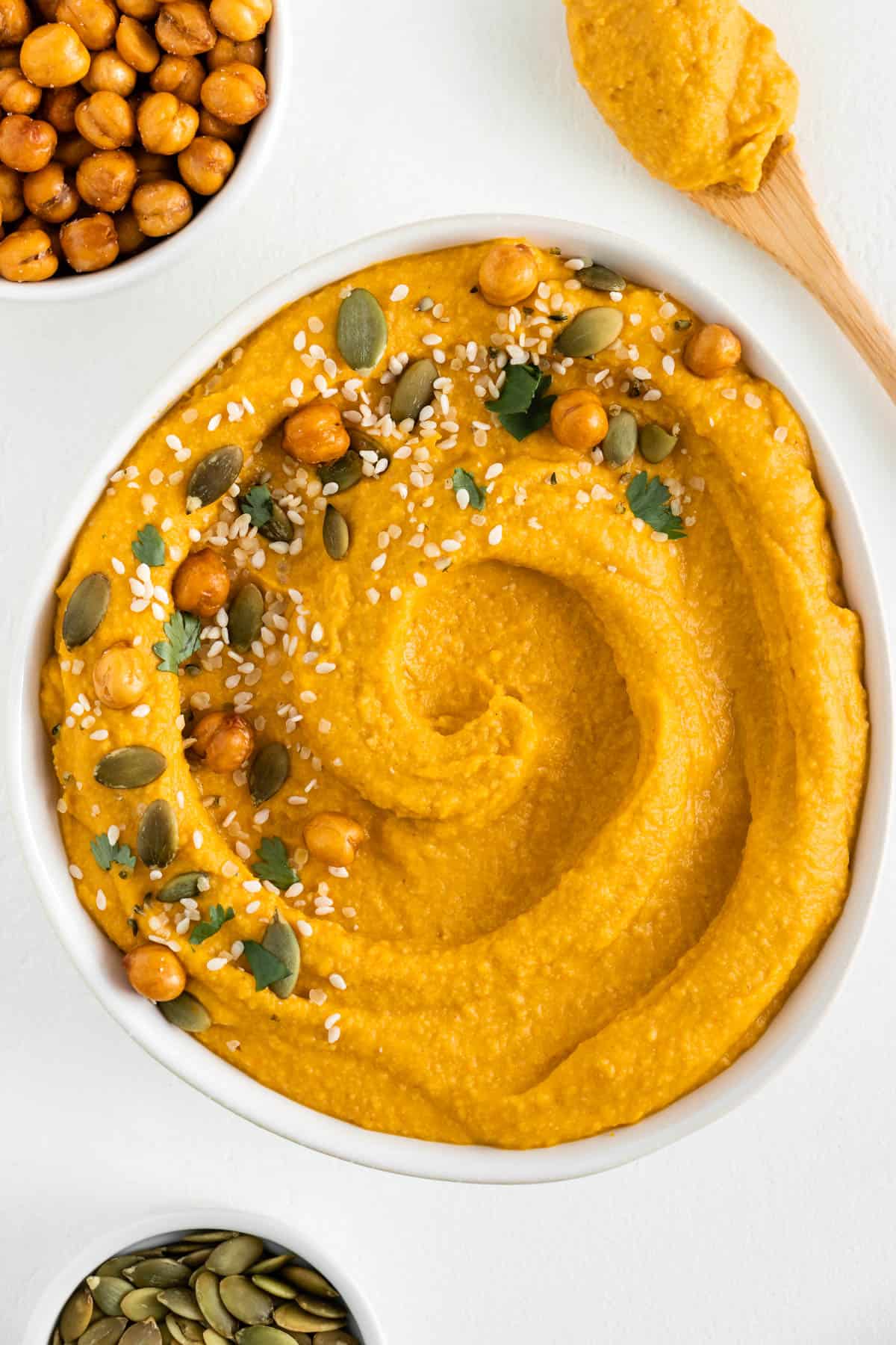 pumpkin hummus in a white bowl surrounded by roasted chickpeas and pumpkin seeds