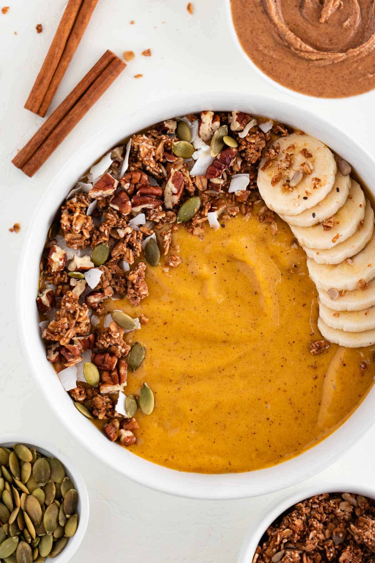 a pumpkin pie smoothie inside a white bowl topped with granola, banana, pumpkin seeds, and coconut flakes