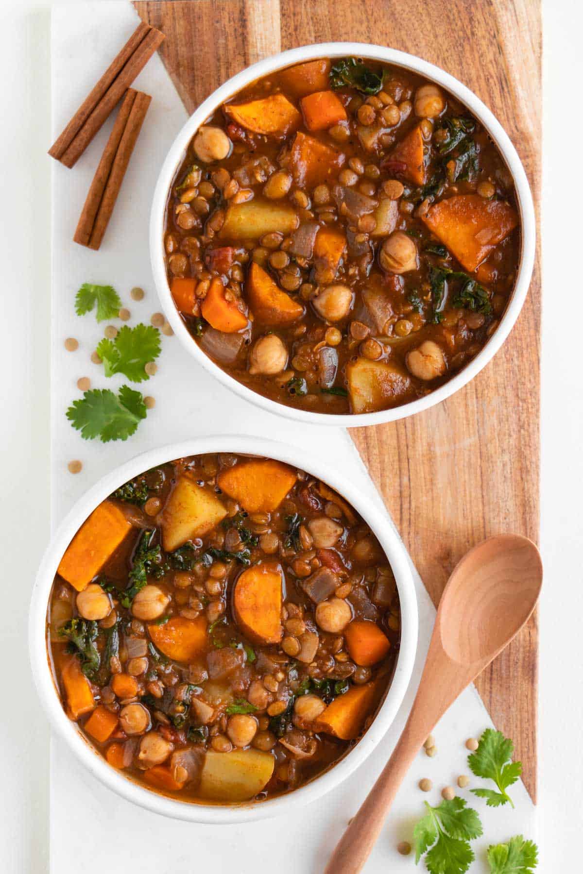 two bowls of vegan moroccan stew on a marble and wood cutting board