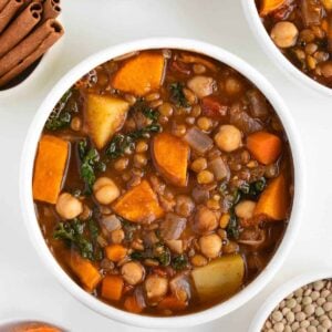 vegan moroccan stew inside two bowls beside fresh cilantro, green lentils, cinnamon, and sliced sweet potato