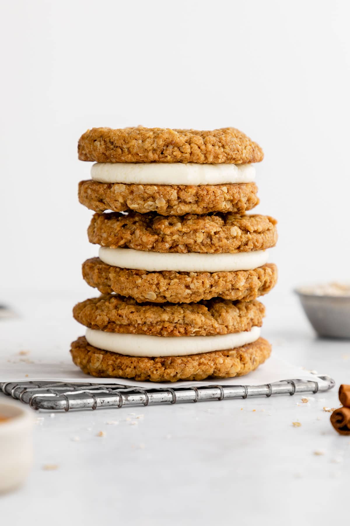 a stack of two vegan oatmeal cream pie cookies beside a jar of almond milk, a bowl of oats, and cinnamon