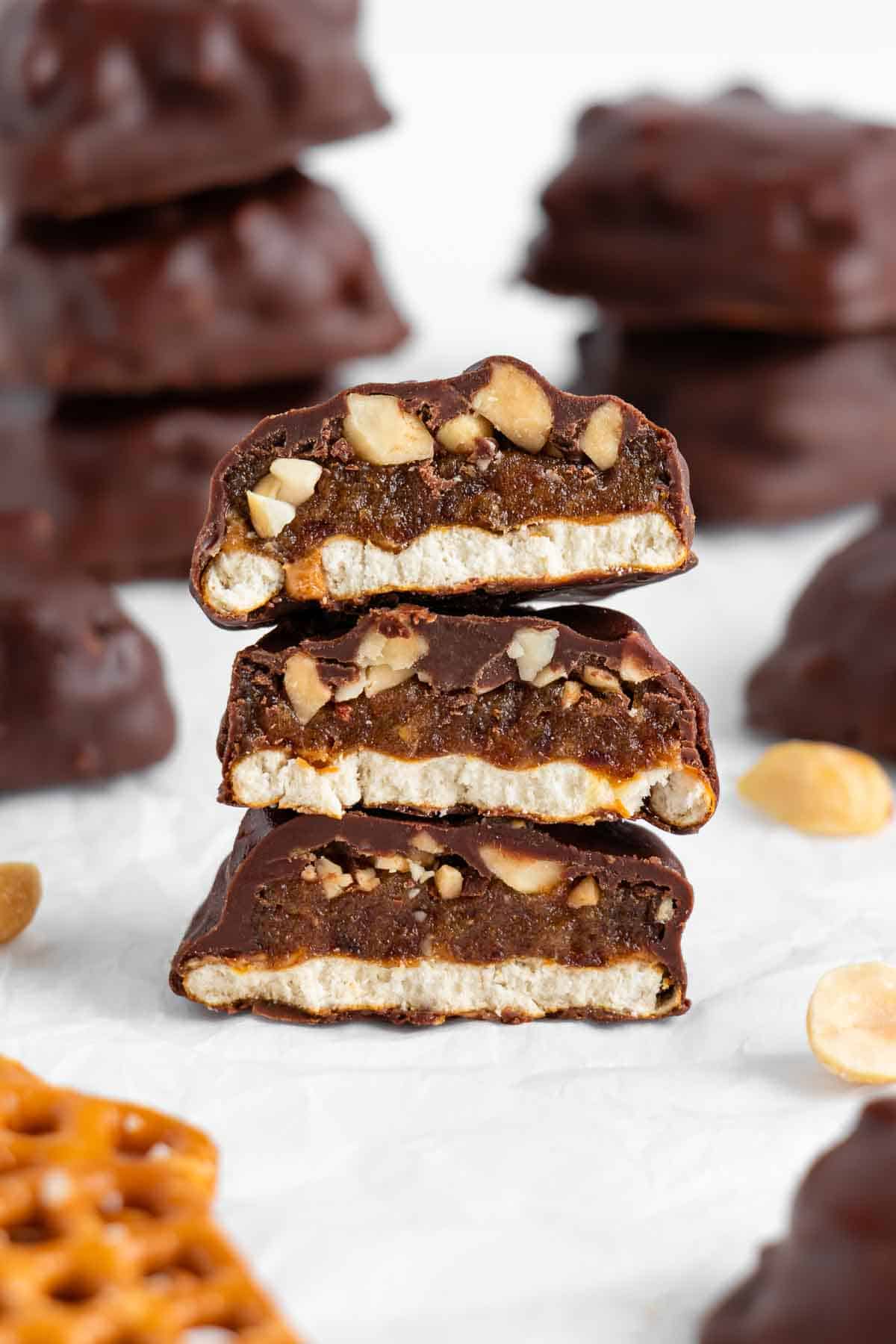 three vegan homemade take 5 candy bars stacked on top of each other, surrounded by chopped peanuts, pretzels, and chocolate chips