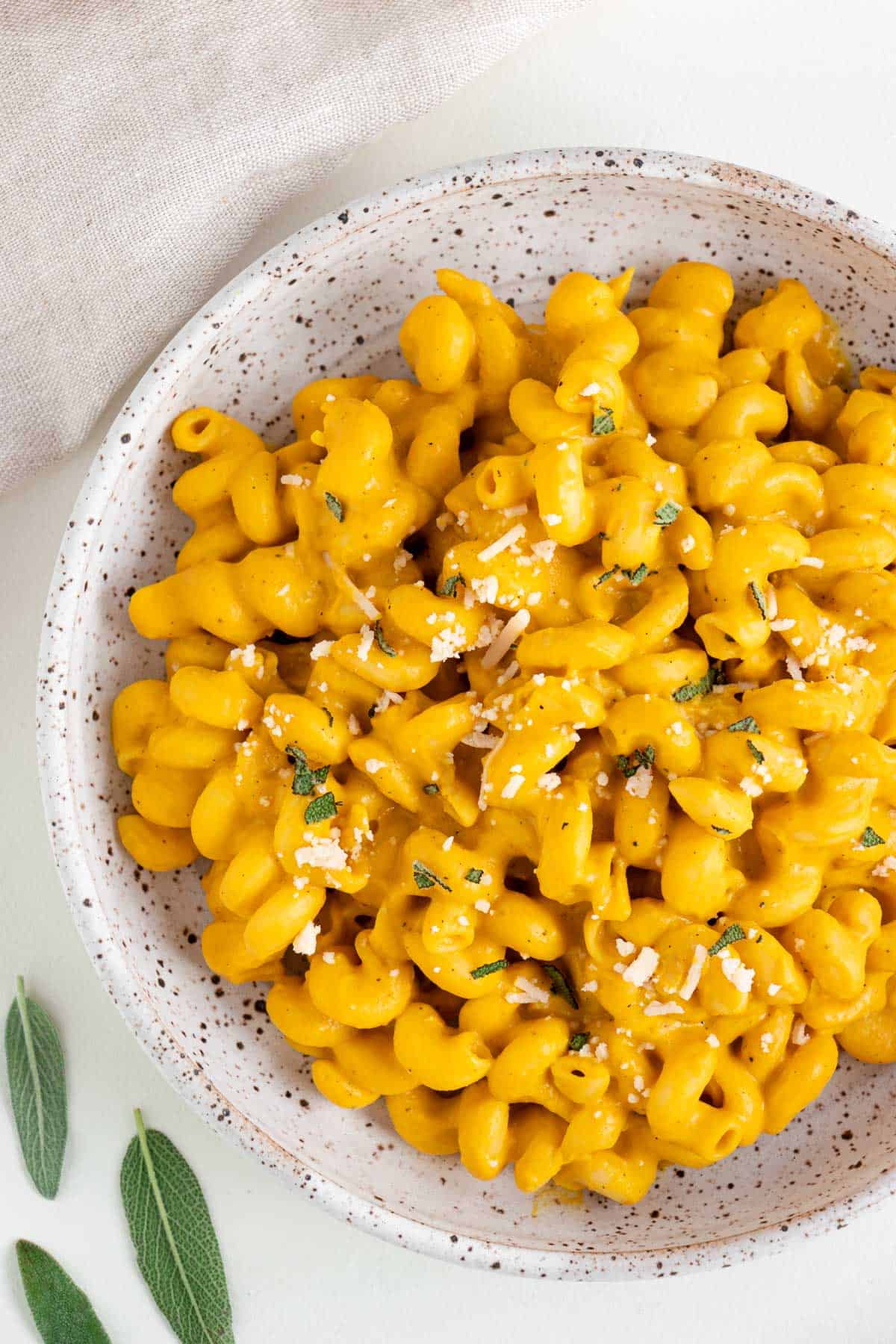 vegan pumpkin pasta in a speckled ceramic bowl with sage and parmesan cheese