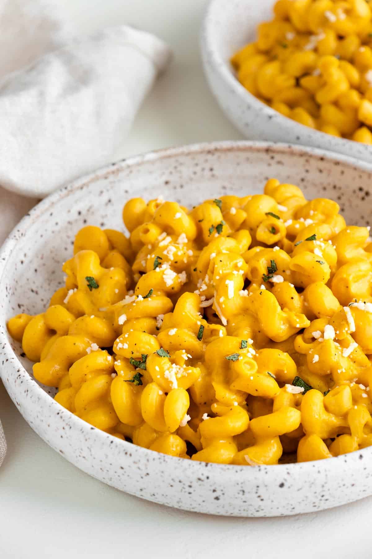 side image of vegan pumpkin pasta inside a ceramic bowl beside a cream-colored linen napkin