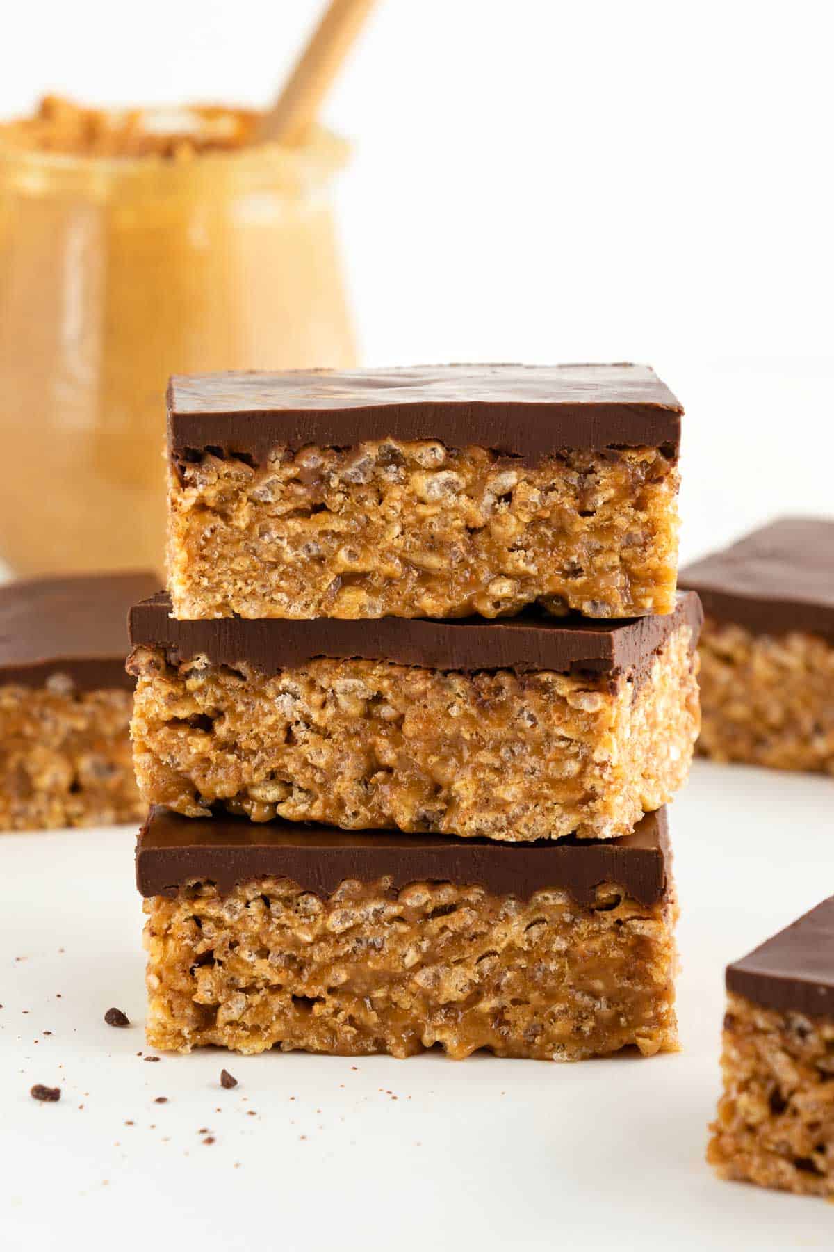 three vegan scotcheroos stacked on top of each other, surrounded by more vegan special k bars and a jar of peanut butter