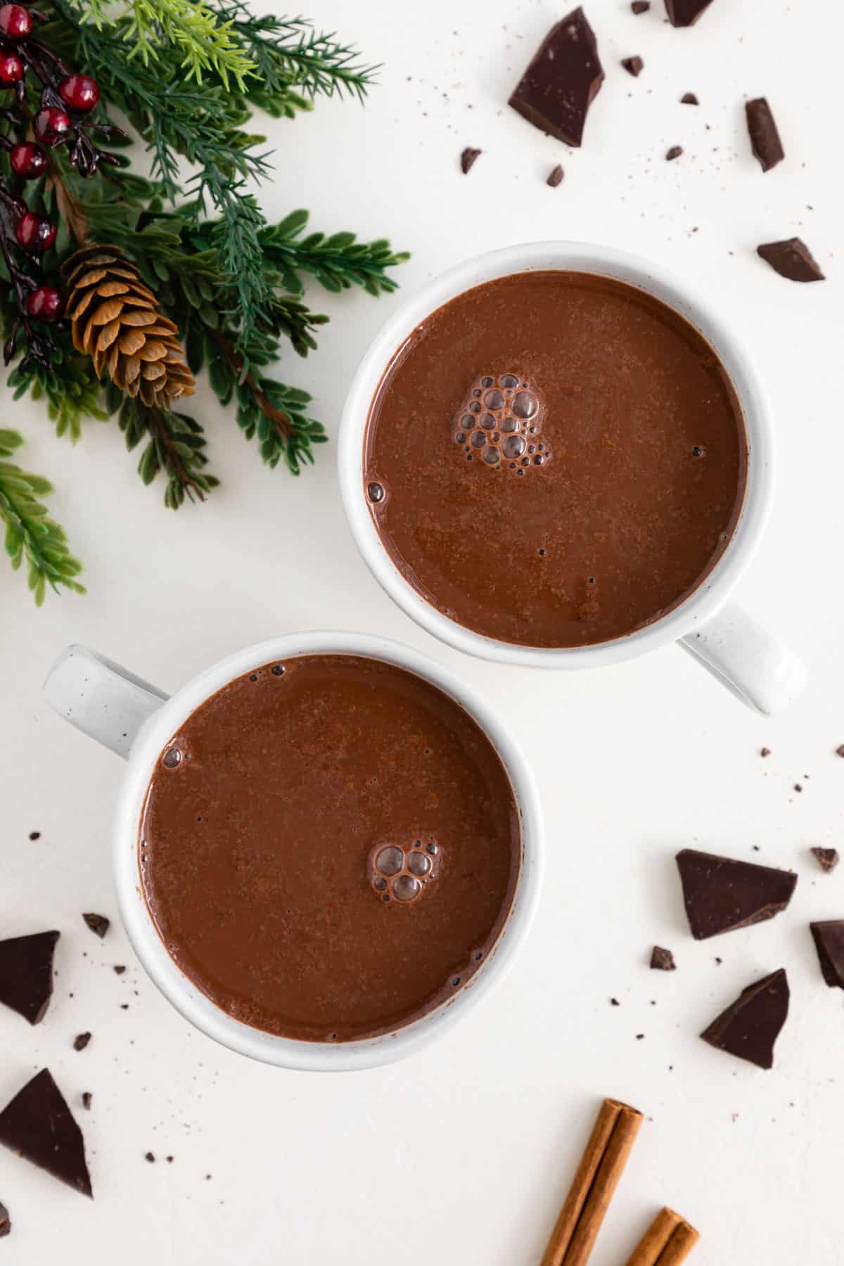 two white mugs filled with vegan hot cocoa, surrounded by broken pieces of dark chocolate