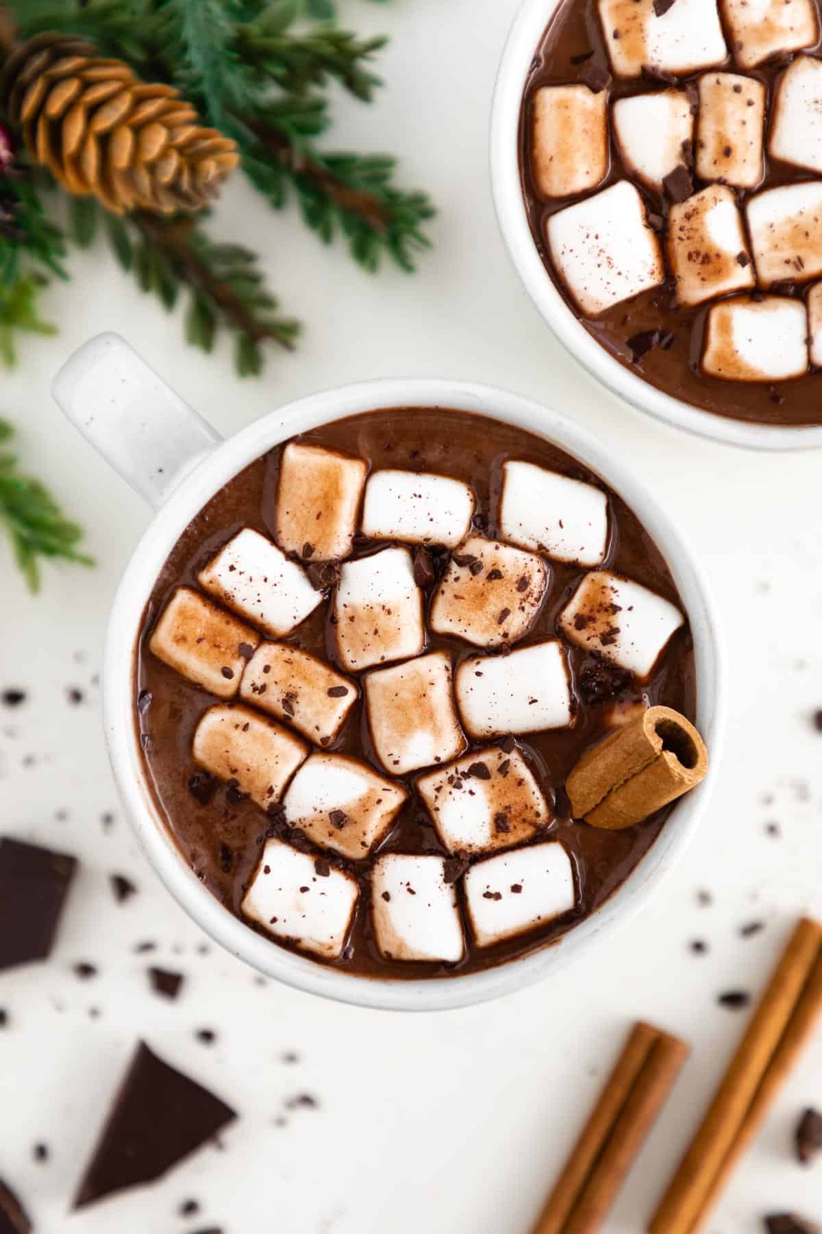 vegan hot chocolate inside a white ceramic mug topped with mini marshmallows and a cinnamon stick