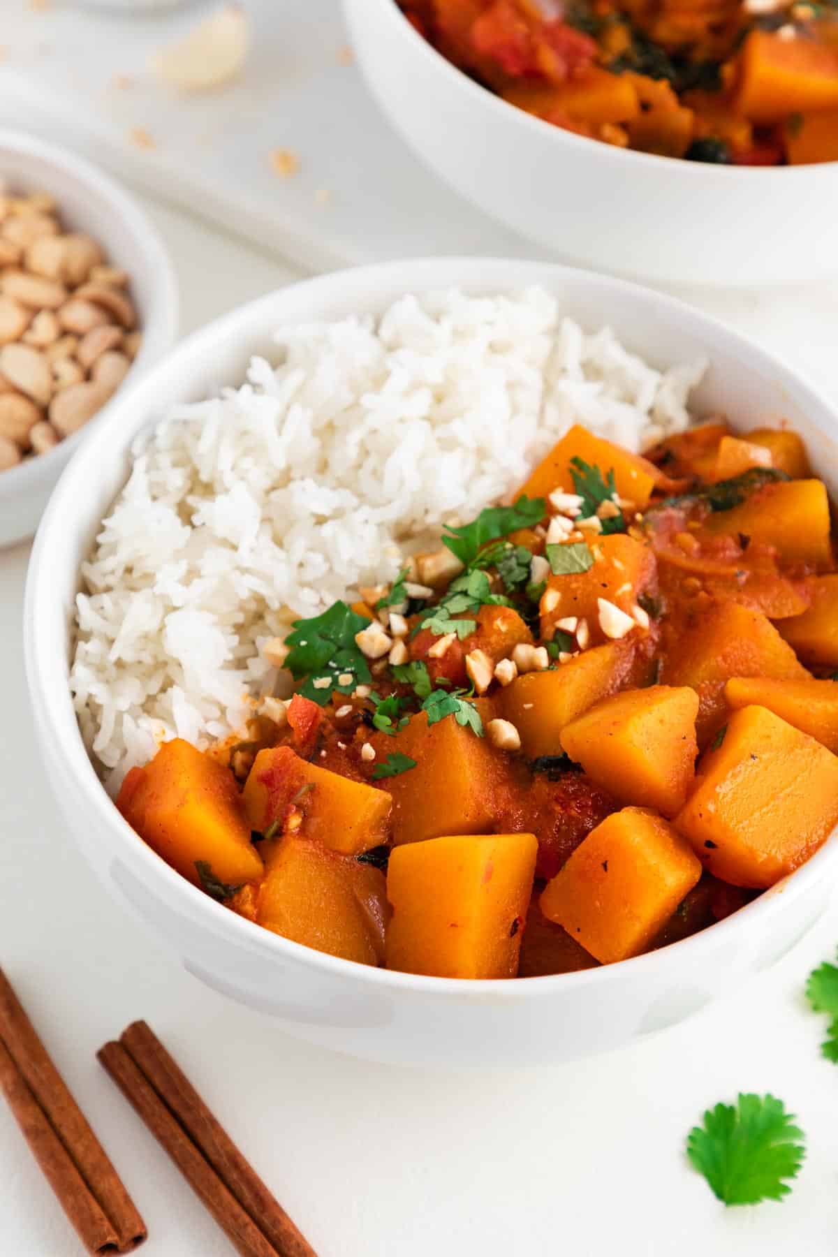 vegan butternut squash curry and white rice in a bowl topped with peanuts and cilantro