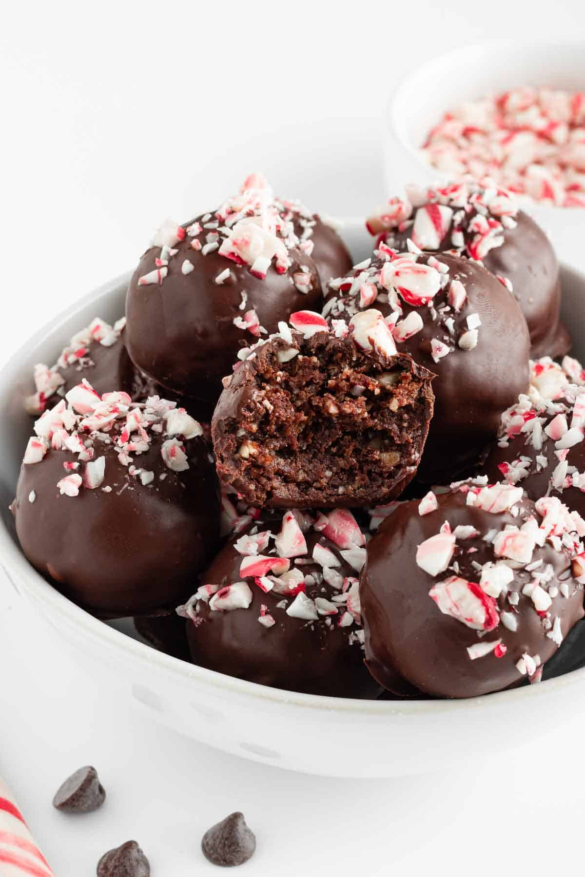 healthy chocolate peppermint truffles stacked in a white bowl with a bite taken out of the middle truffle
