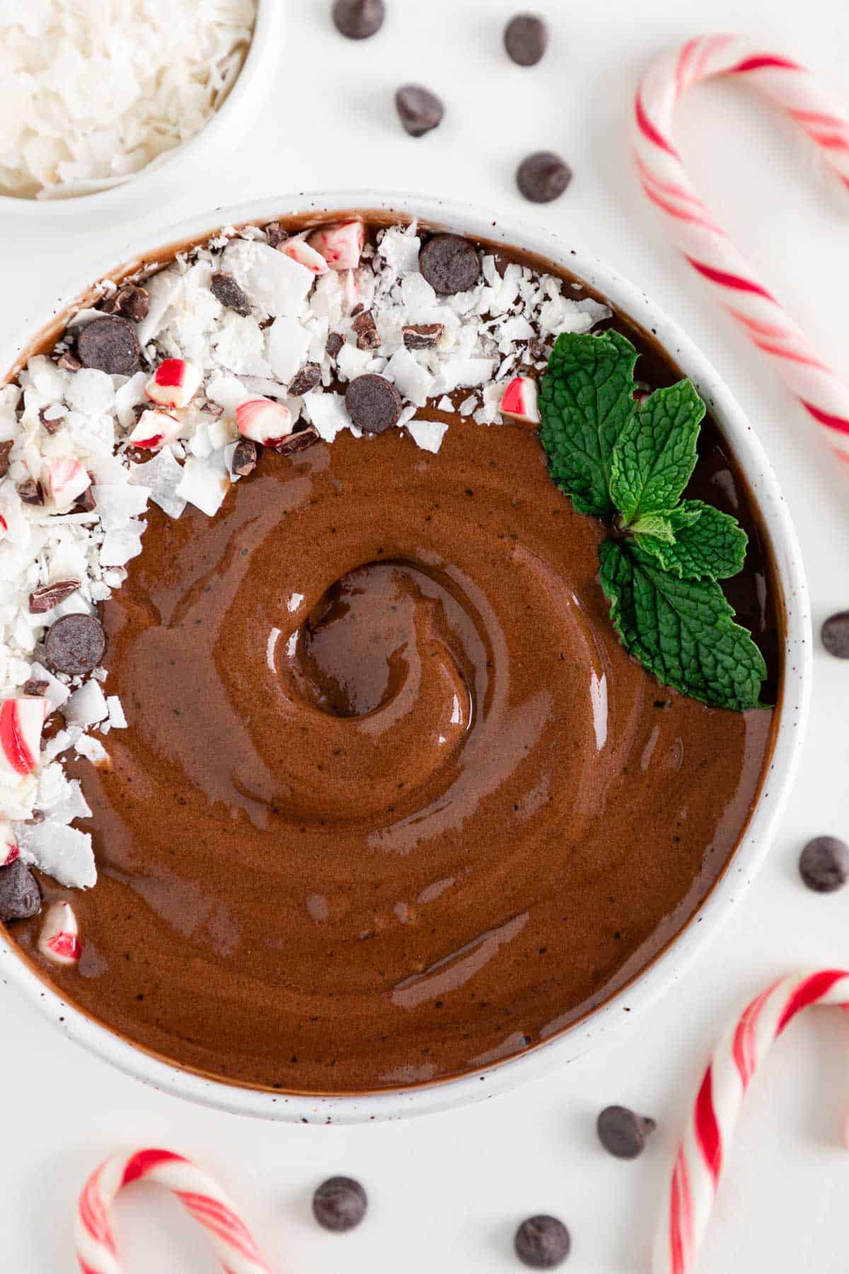a chocolate peppermint mocha smoothie bowl surrounded by candy canes, chocolate chips, and coconut flakes