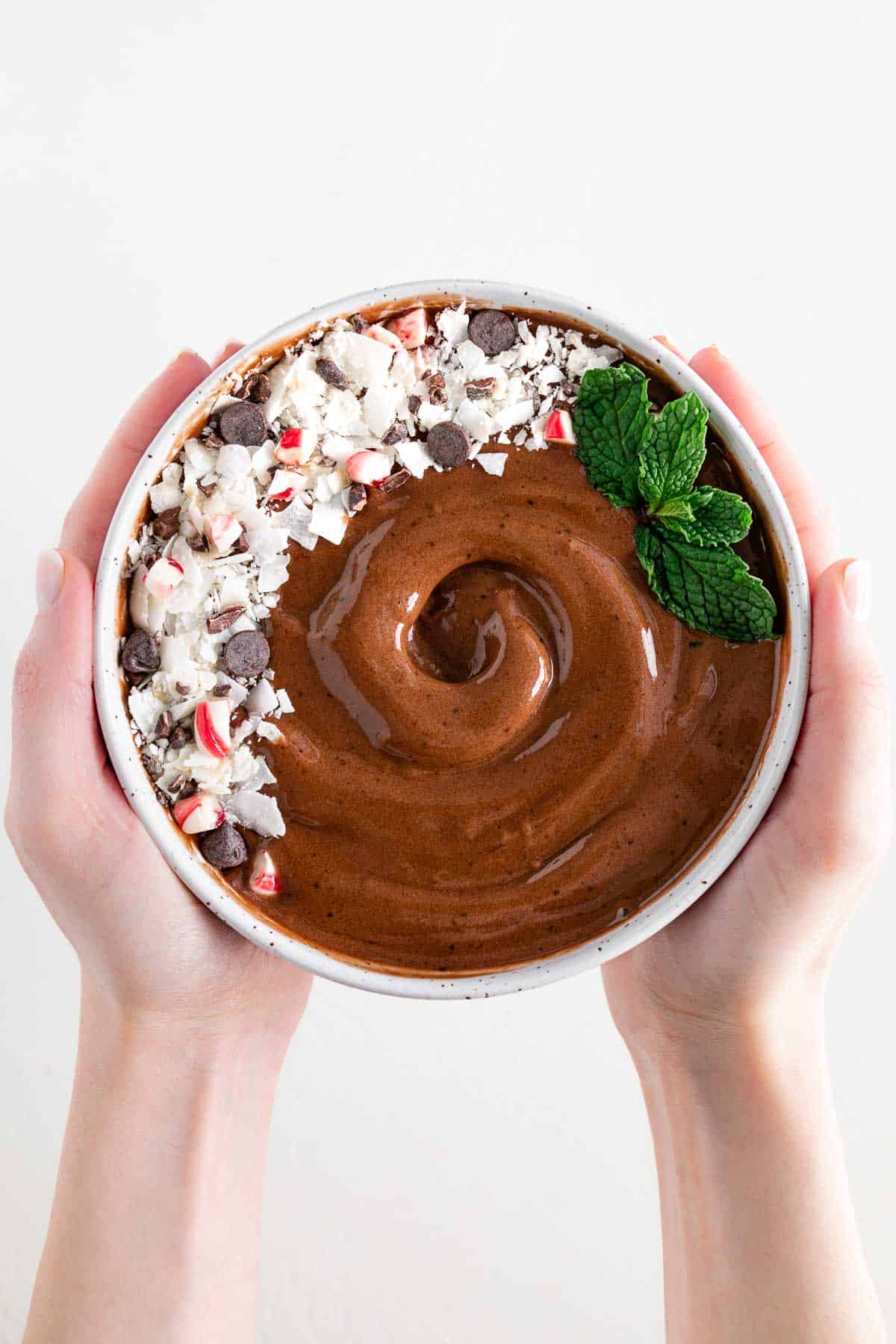 two hands holding a bowl filled with a chocolate peppermint mocha smoothie bowl