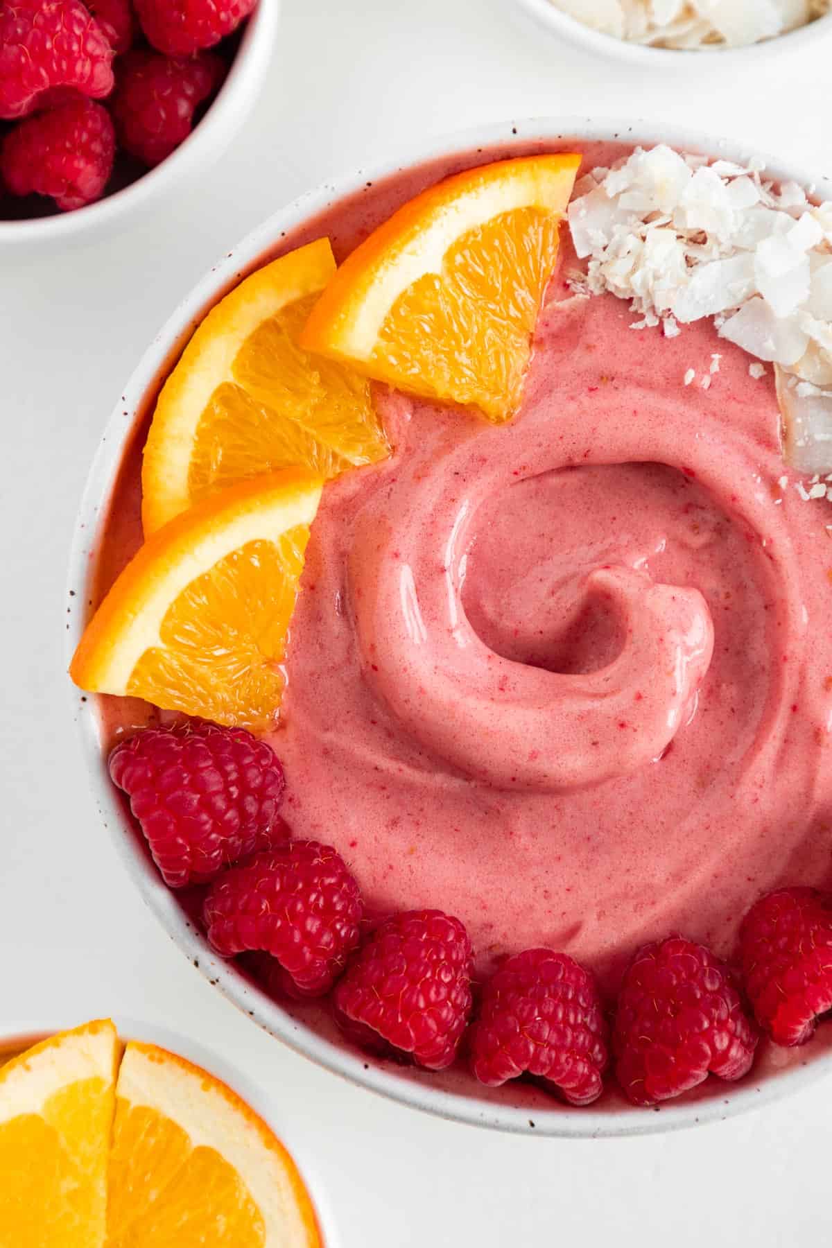 a raspberry smoothie bowl topped with oranges, coconut flakes, and berries