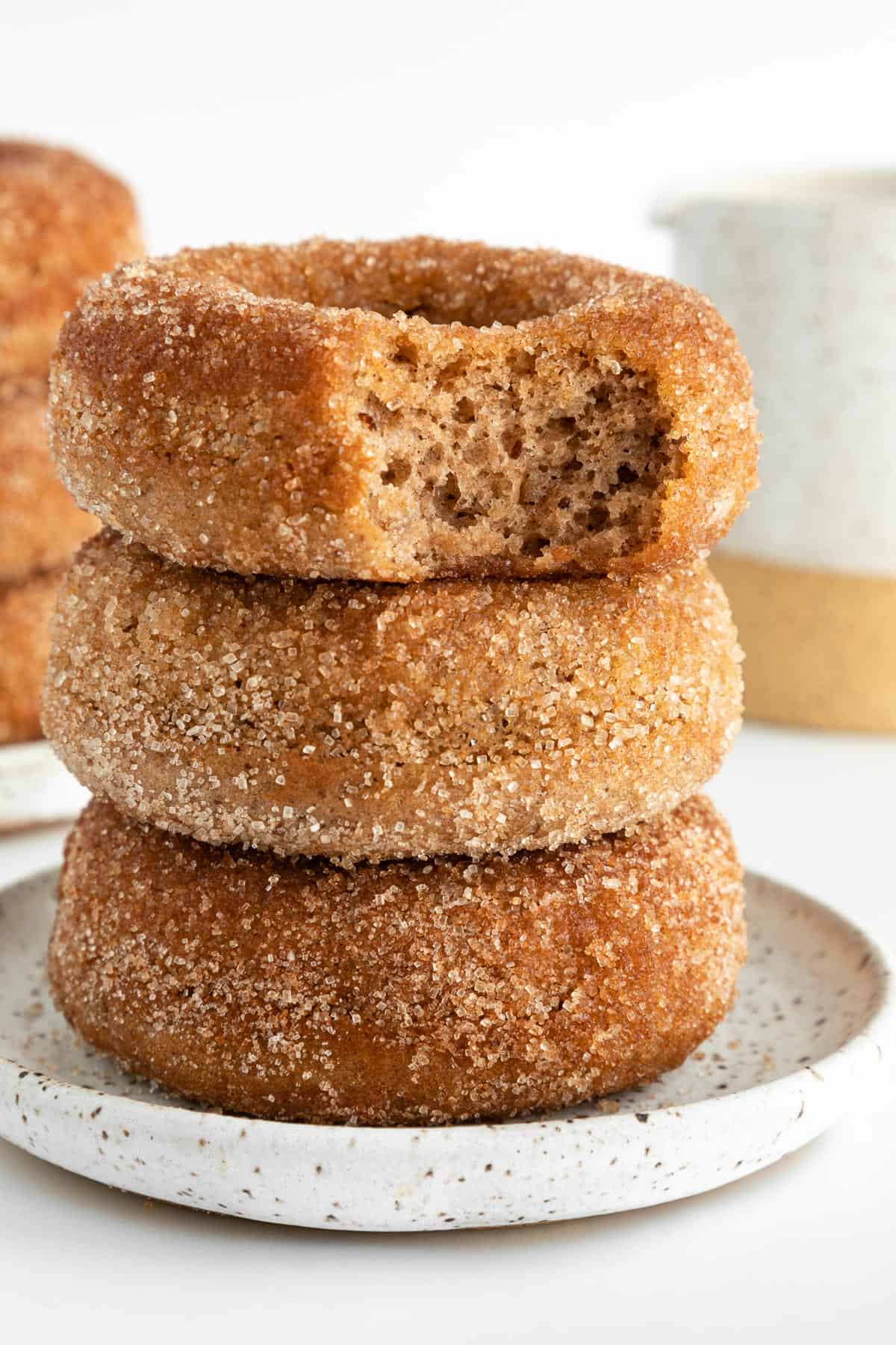 three vegan cinnamon sugar donuts stacked with a bite taken out of the top donut