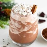 a glass filled with vegan frozen hot chocolate, topped with whipped cream and a cinnamon stick