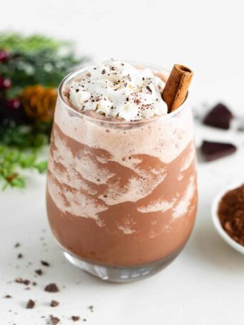 a glass filled with vegan frozen hot chocolate, topped with whipped cream and a cinnamon stick