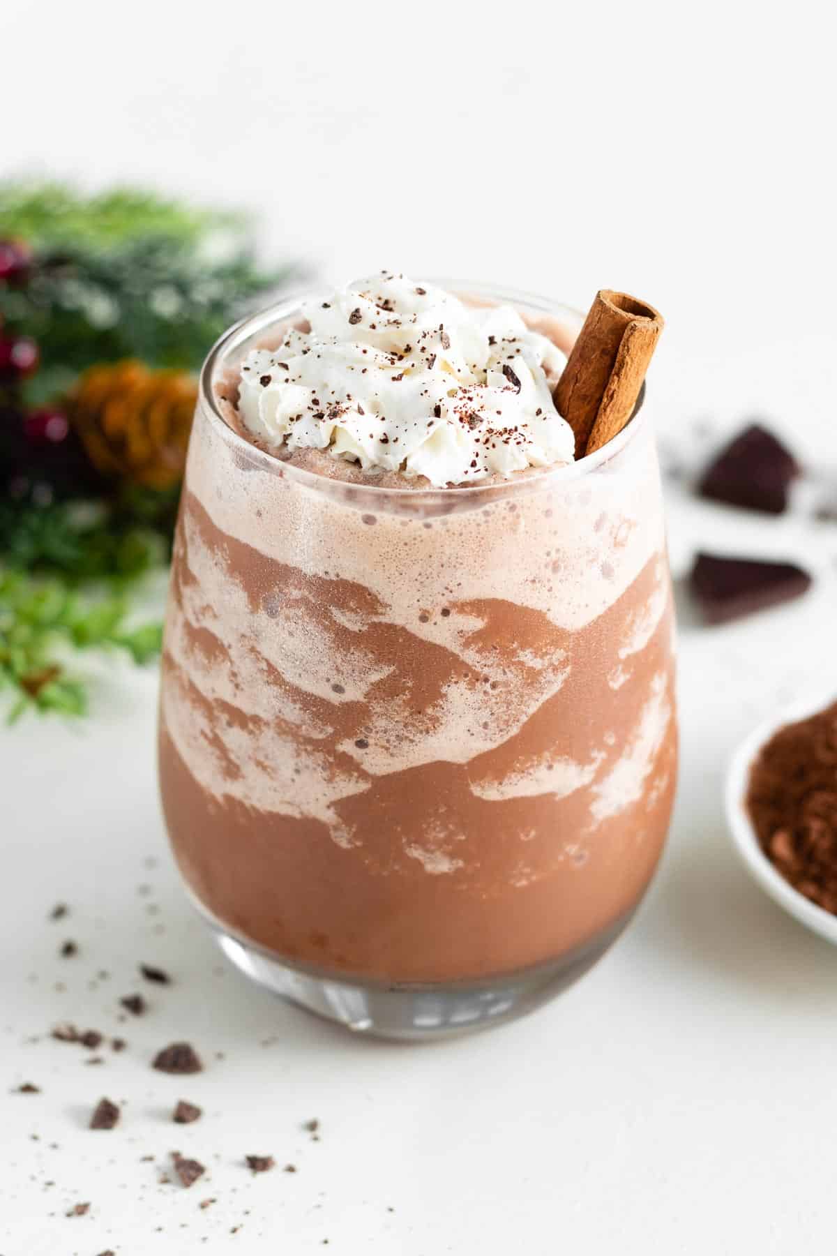 a glass filled with vegan frozen hot chocolate, topped with whipped cream and a cinnamon stick