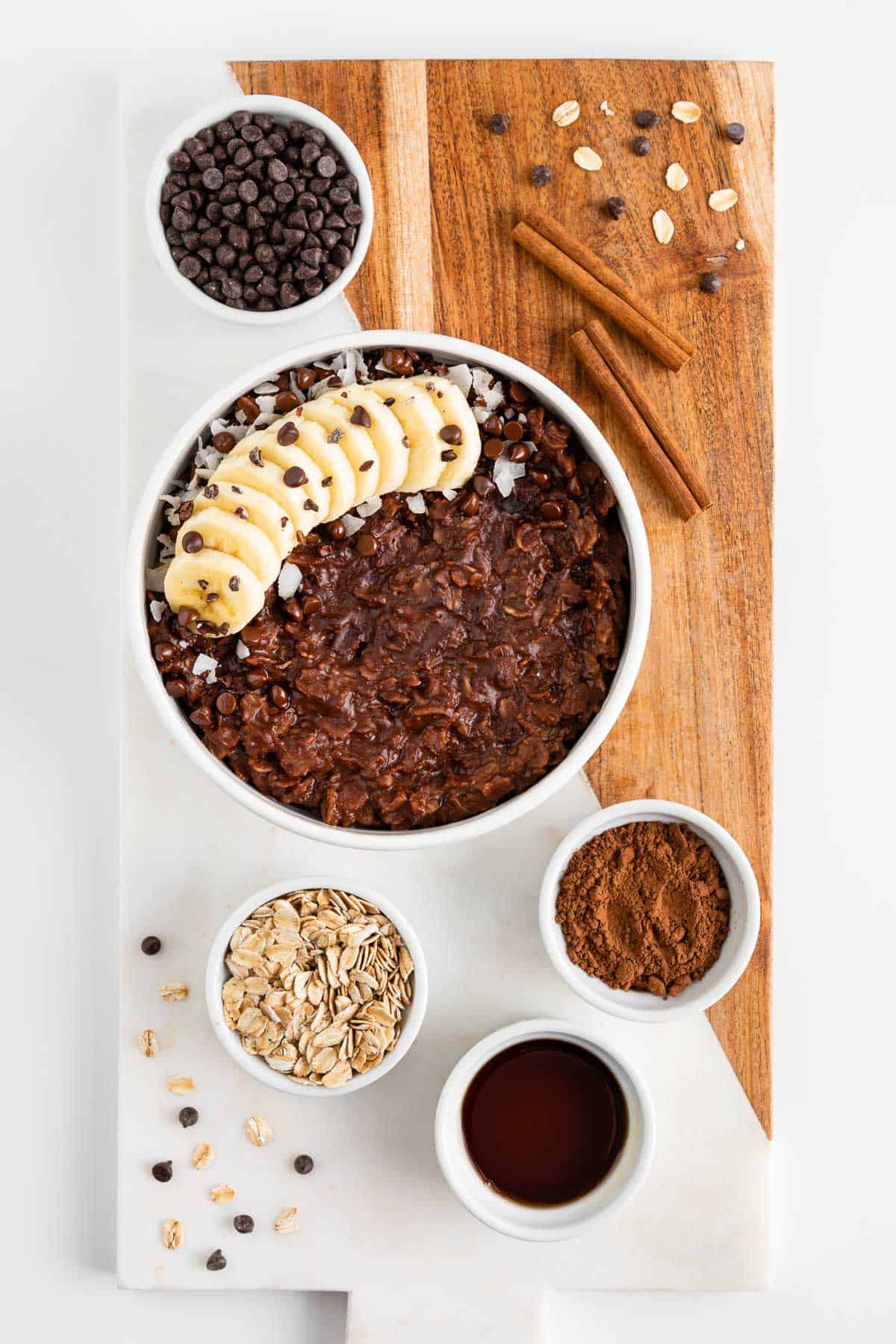 a marble and wood cutting board topped with vegan chocolate oatmeal and small bowls filled with the ingredients