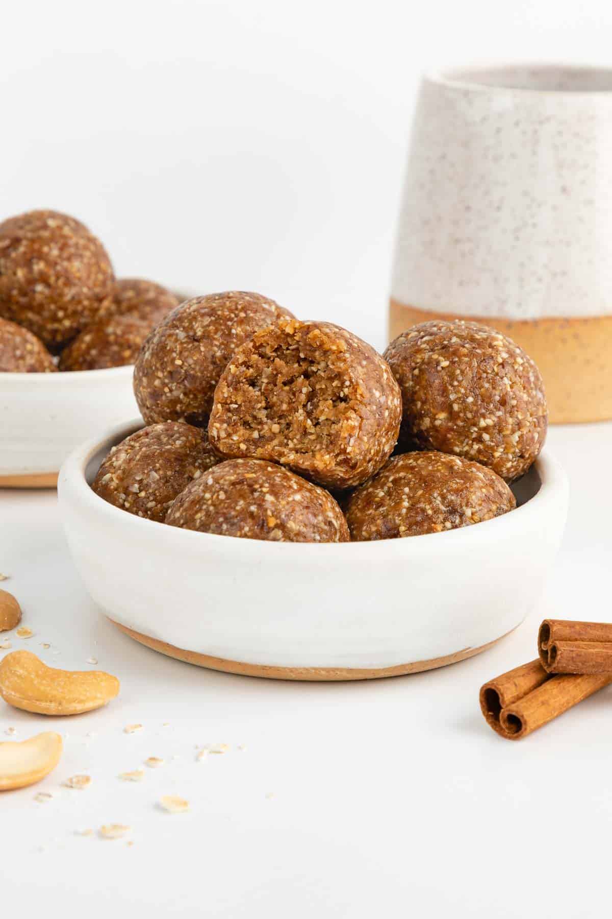 cinnamon roll energy balls stacked inside a small white bowl with a bite taken out of the middle ball