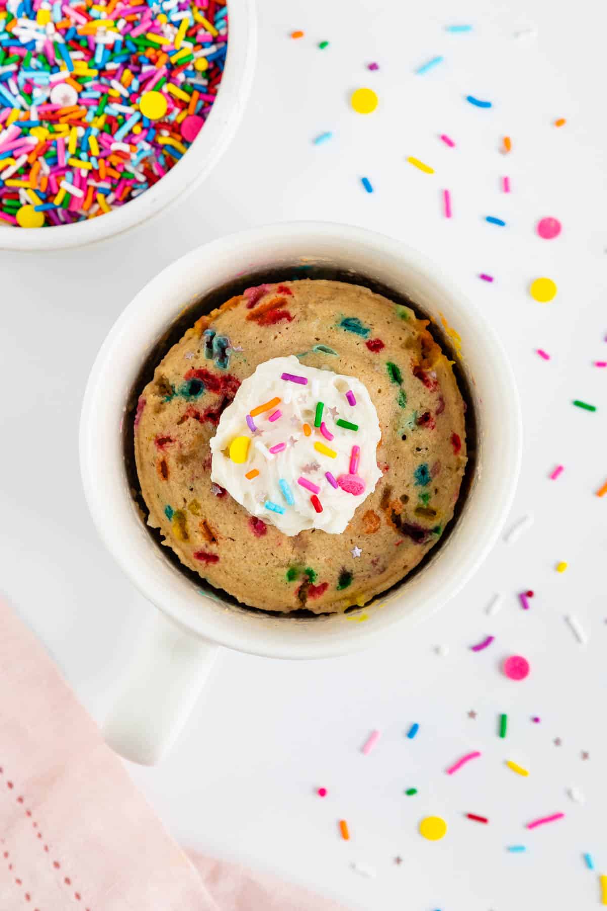 a vegan funfetti mug cake inside a white mug topped with a dollop of vanilla frosting and sprinkles