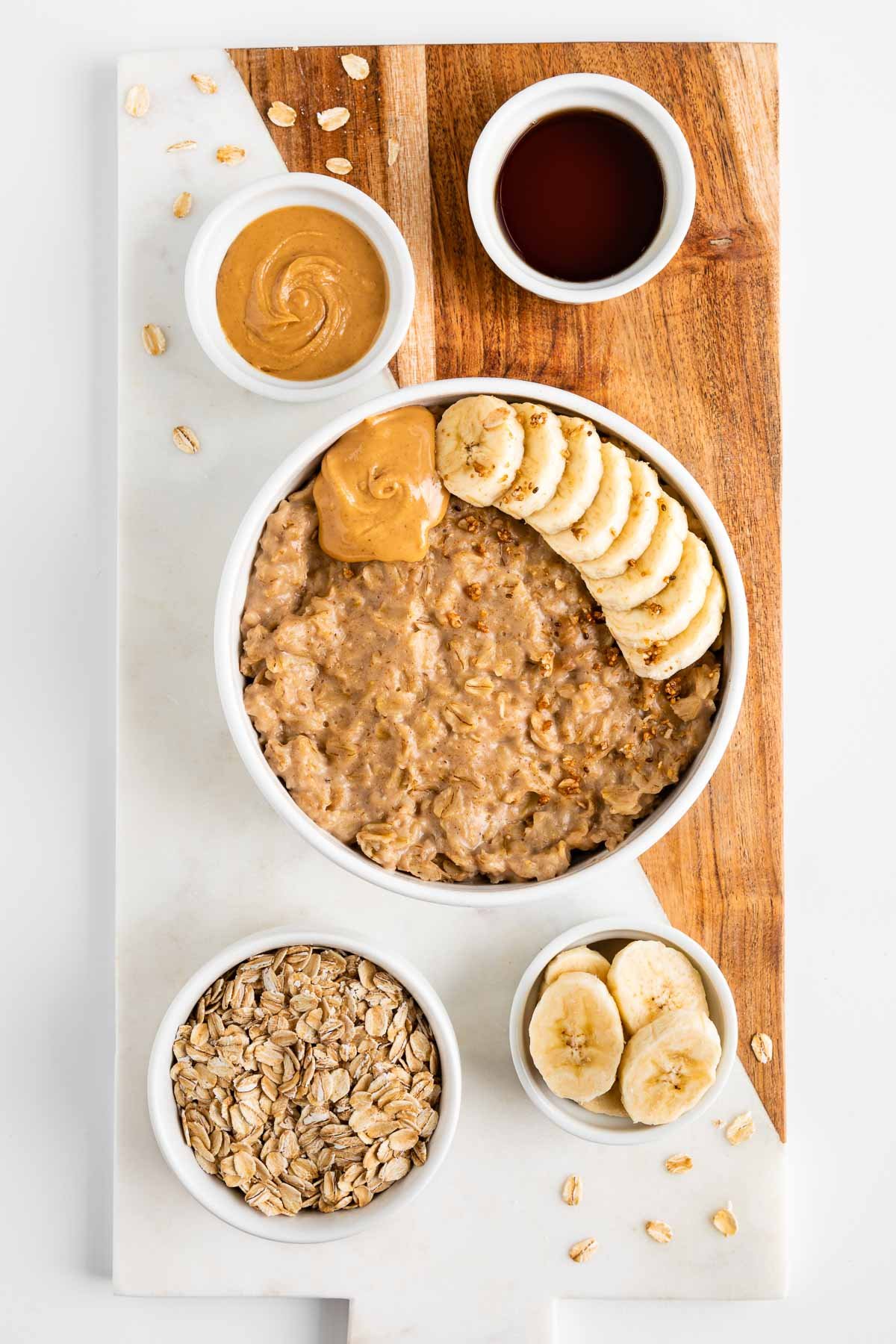 a marble and wood cutting board topped with a bowl of peanut butter oatmeal and small bowls filled with the ingredients in the recipe