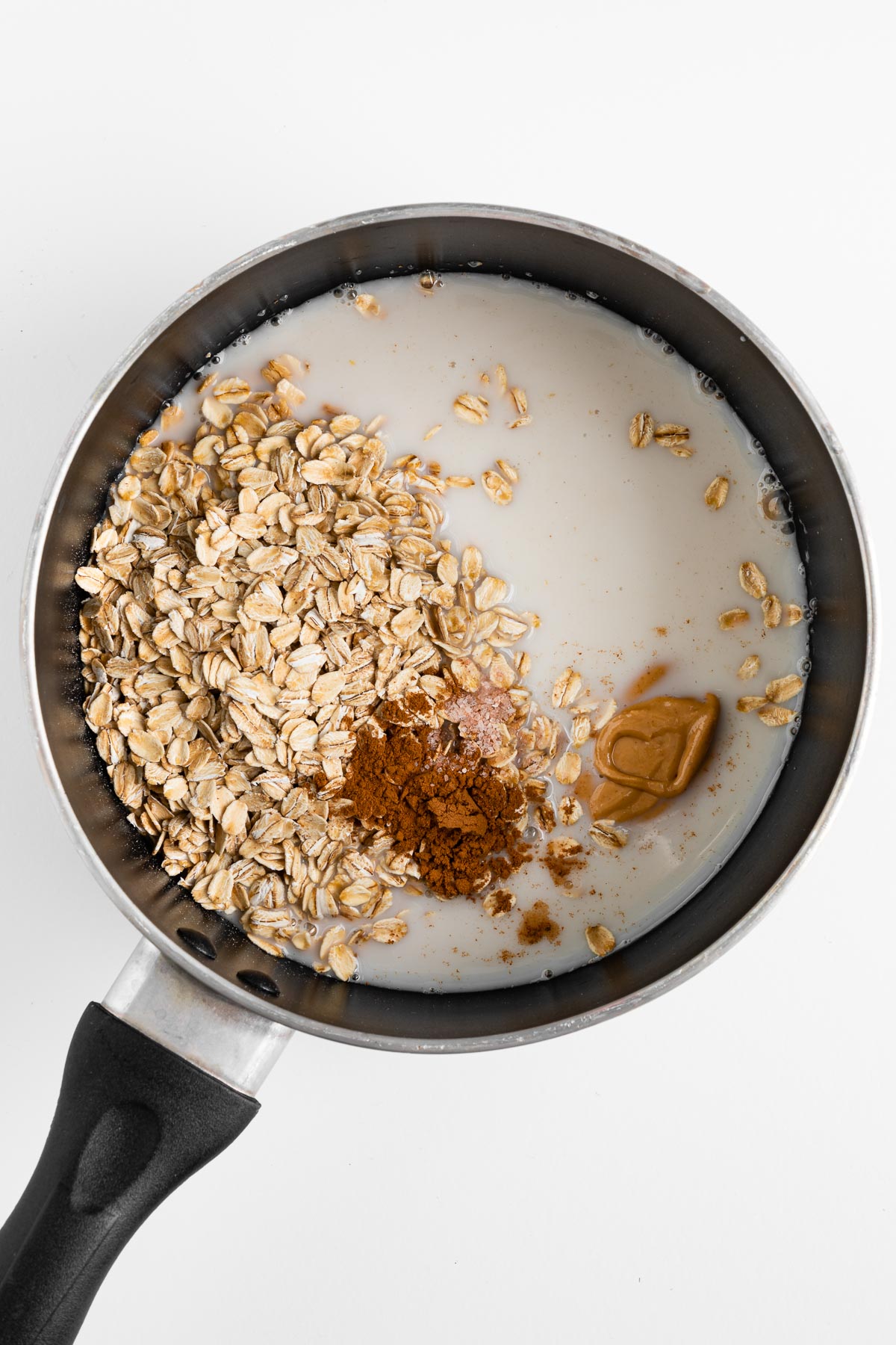 rolled oats, almond milk, cinnamon, and nut butter inside a small saucepan