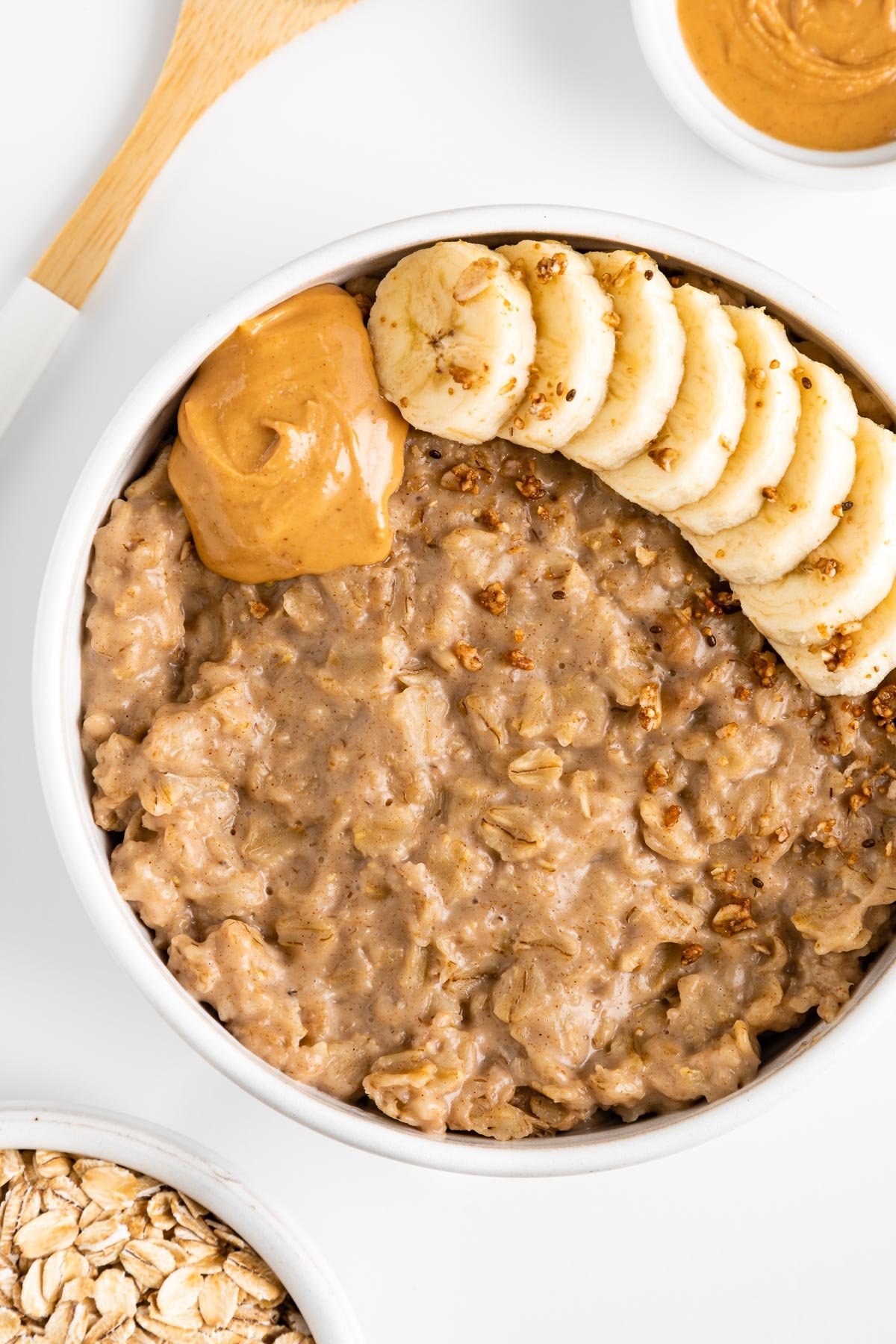 peanut butter oatmeal in a white bowl, topped with sliced banana, granola, and nut butter