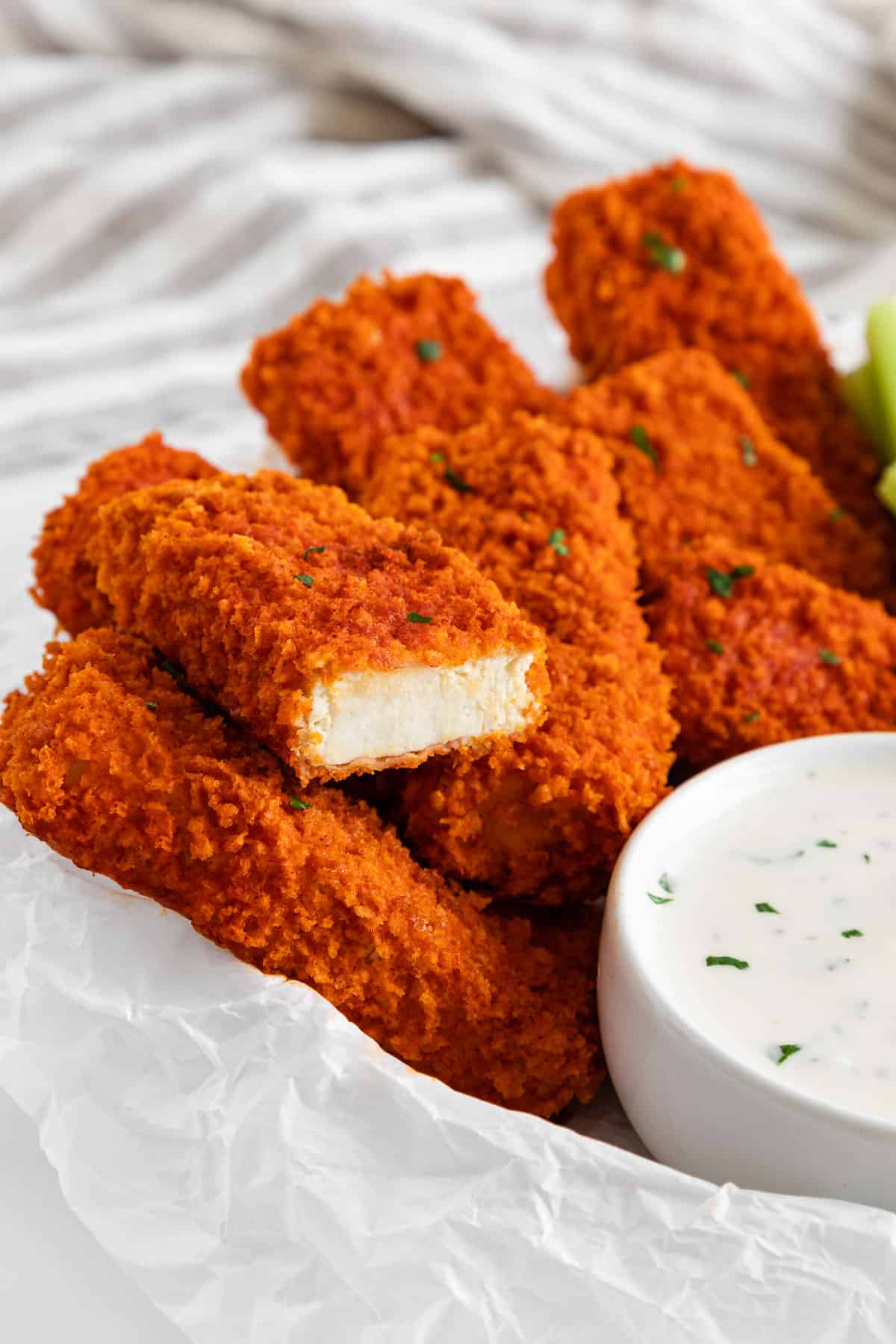 vegan buffalo tofu wings spread on a plate with a bite taken out of one of the wings