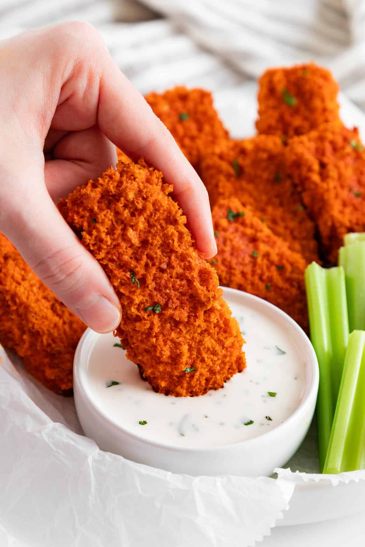 a left hand holding a vegan buffalo tofu wing, dipping it into a bowl of ranch dressing