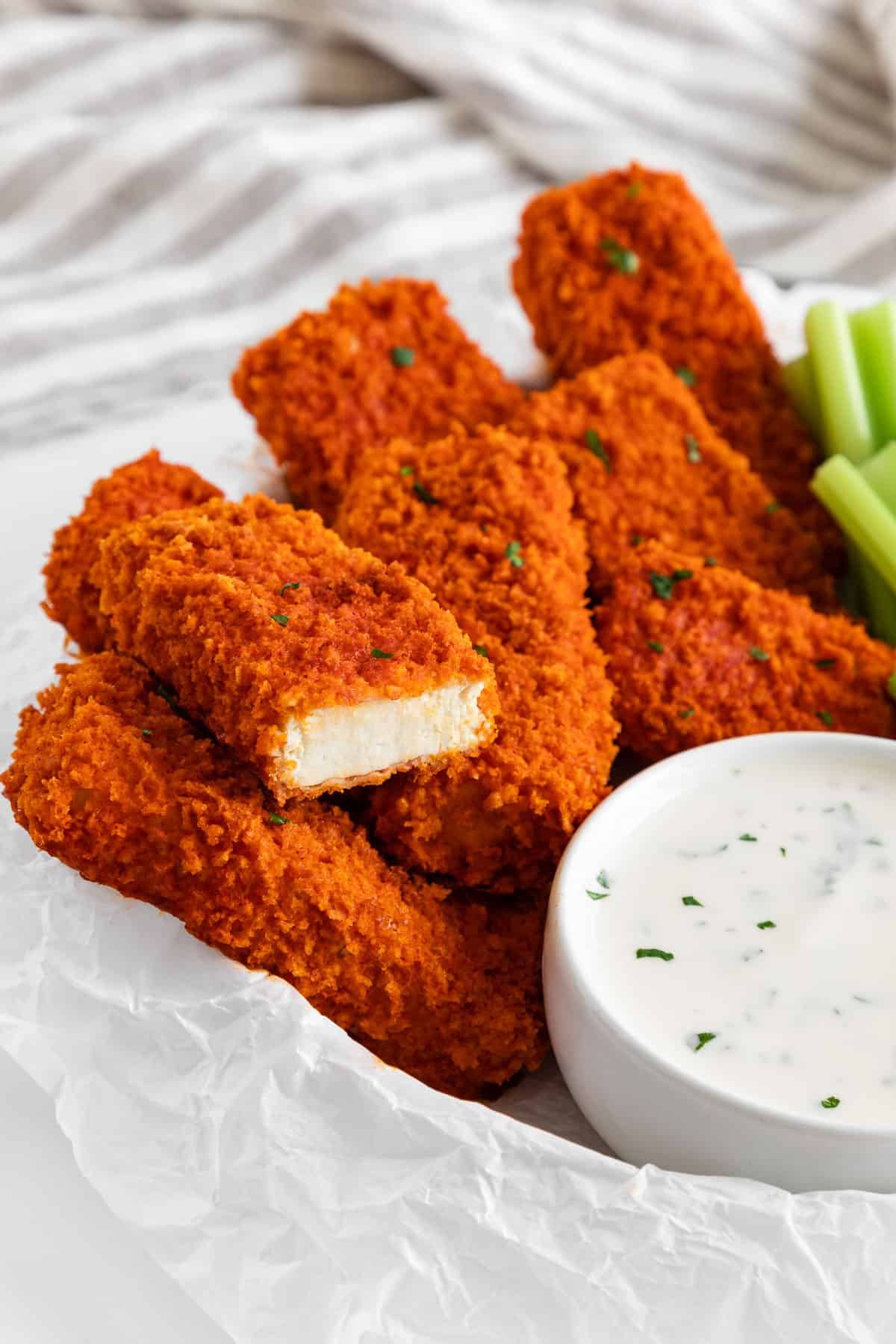 vegan buffalo tofu wings spread on a plate with a bite taken out of one of the wings